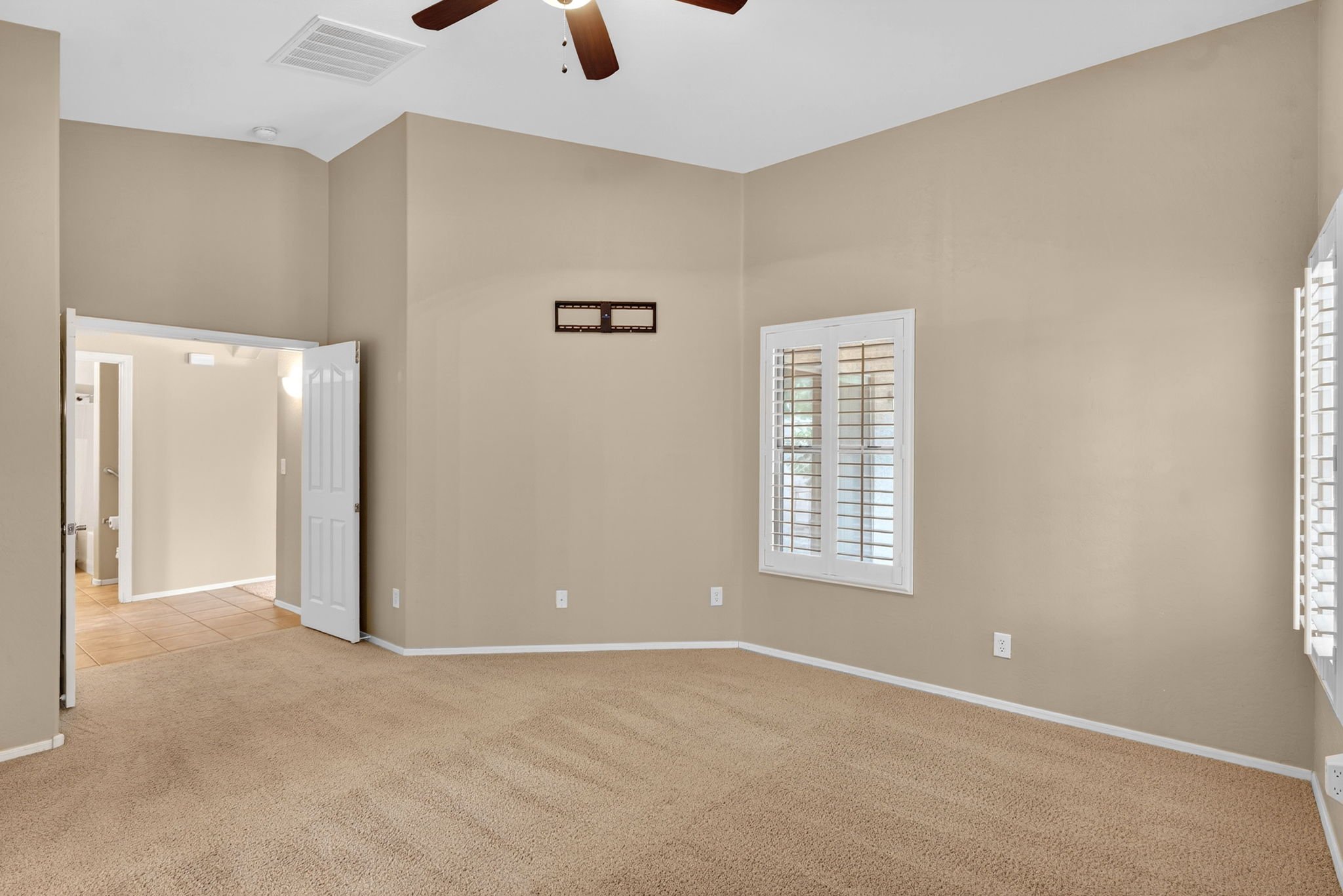Empty living room with beige carpet, beige walls, white trim, and windows with white blinds.