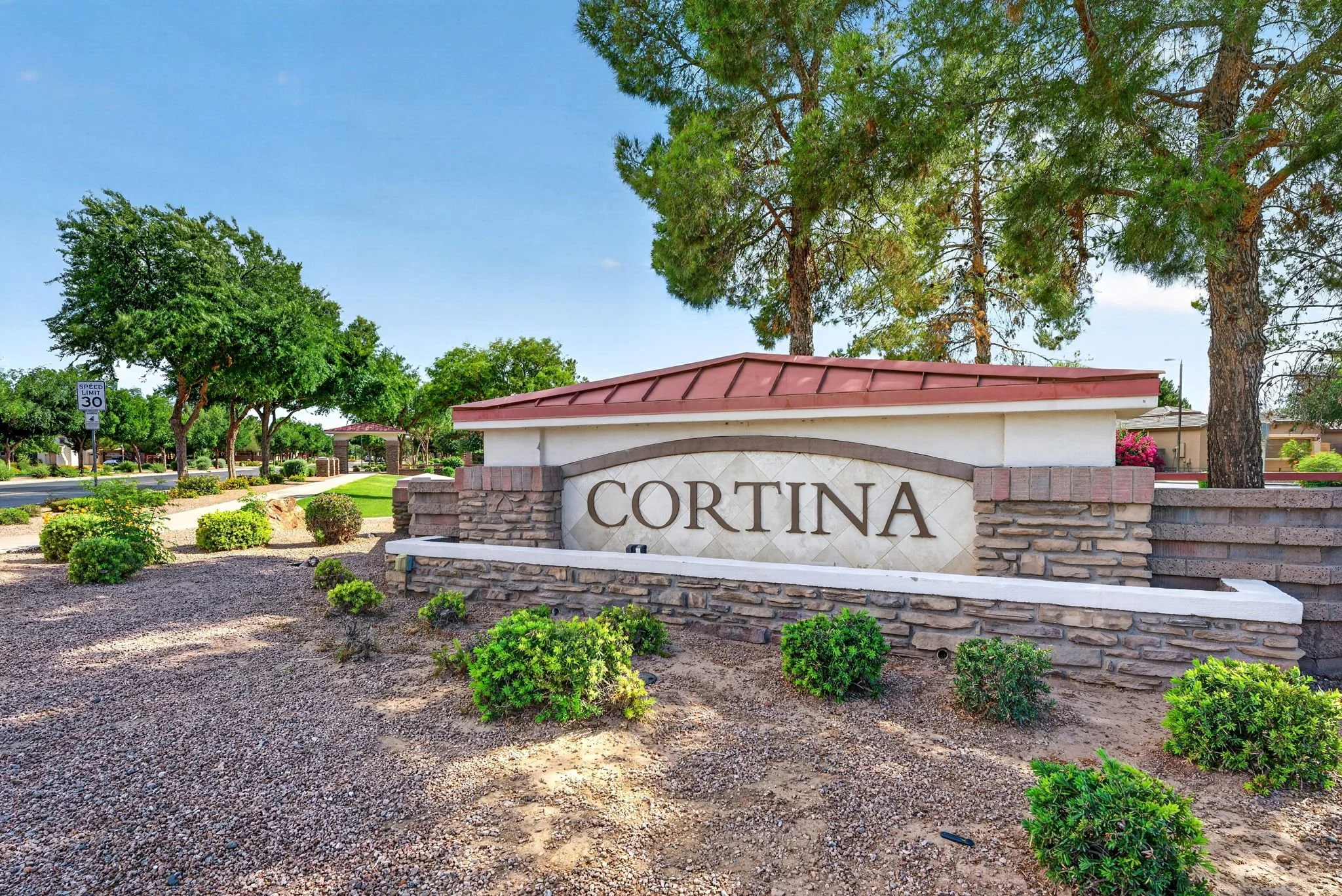 Entrance sign for Cortina neighborhood with landscaping and trees, under a clear blue sky.