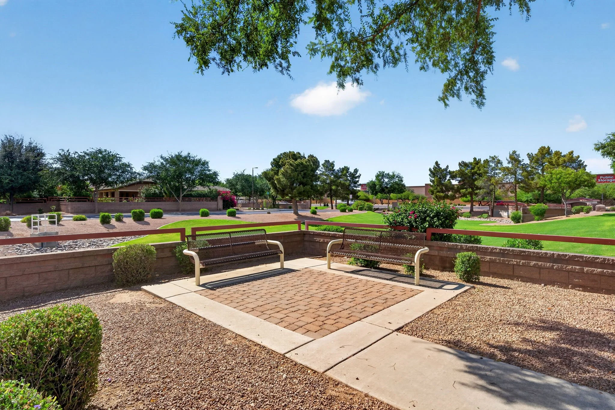 Public park with benches, trees, bushes, and a clear blue sky.