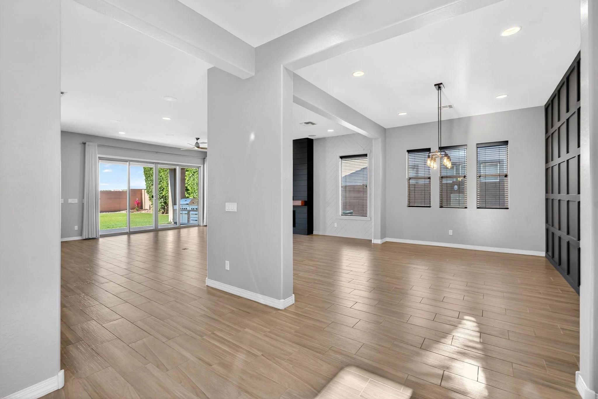 Empty modern living room with large windows, sliding glass door, wooden flooring, white walls, and a ceiling fan.