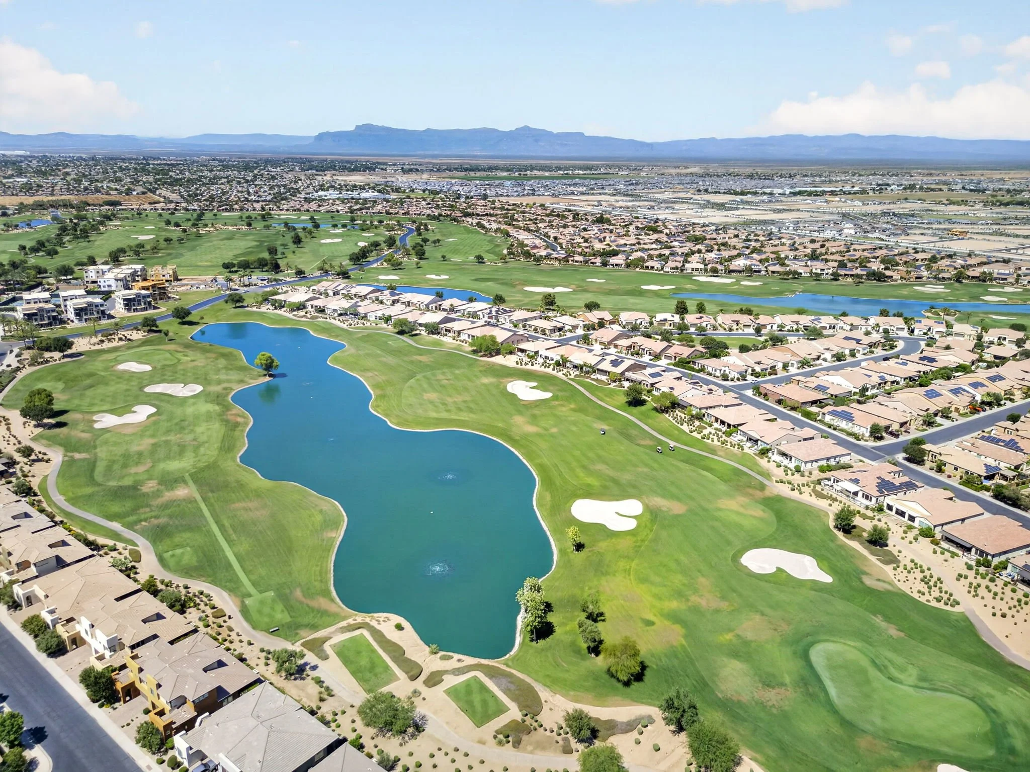 Aerial view of a golf course with water hazards, sand bunkers, surrounding residential neighborhood, and distant mountains in the background.