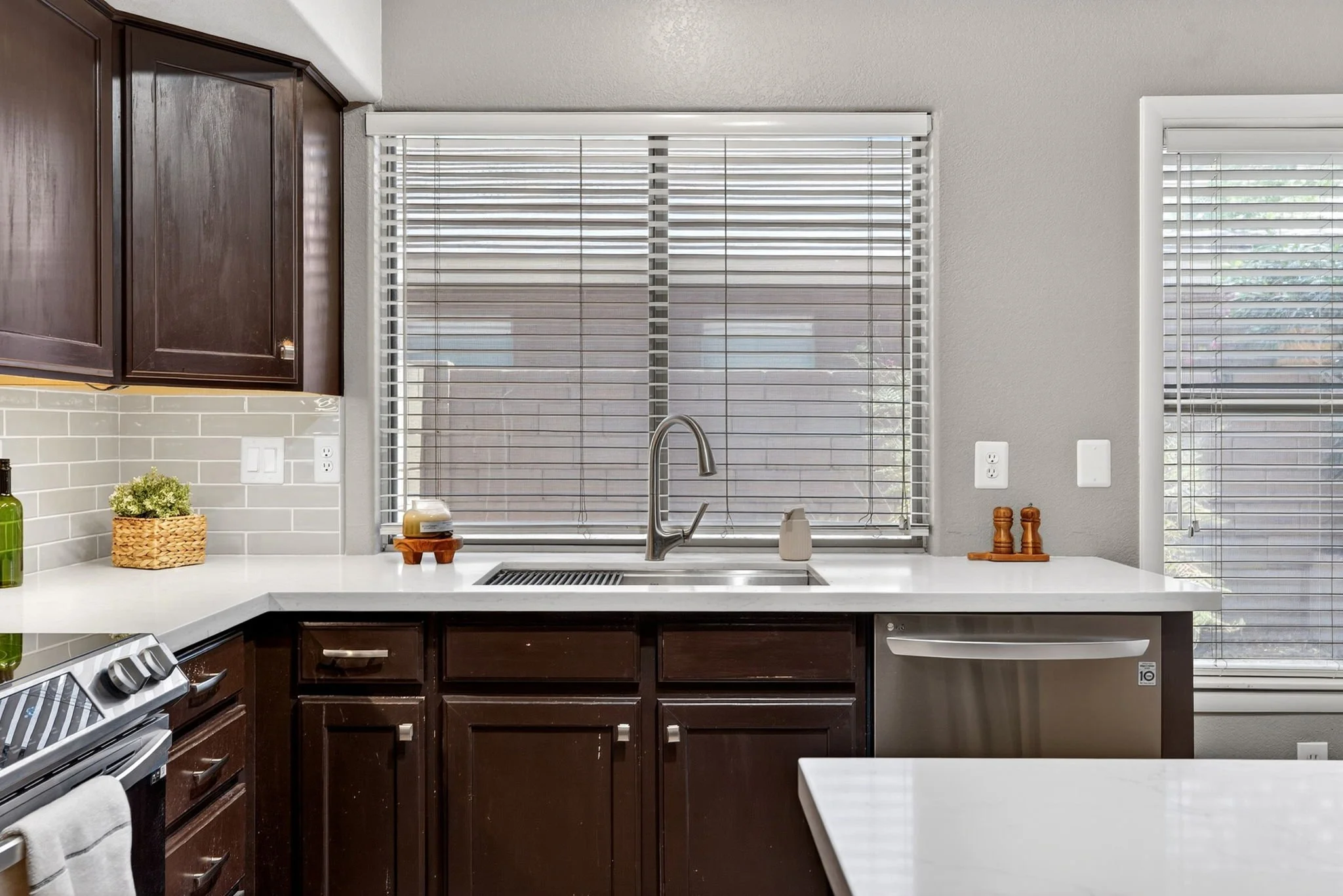 Kitchen with dark wood cabinets, a white countertop, and a window with blinds above the sink.