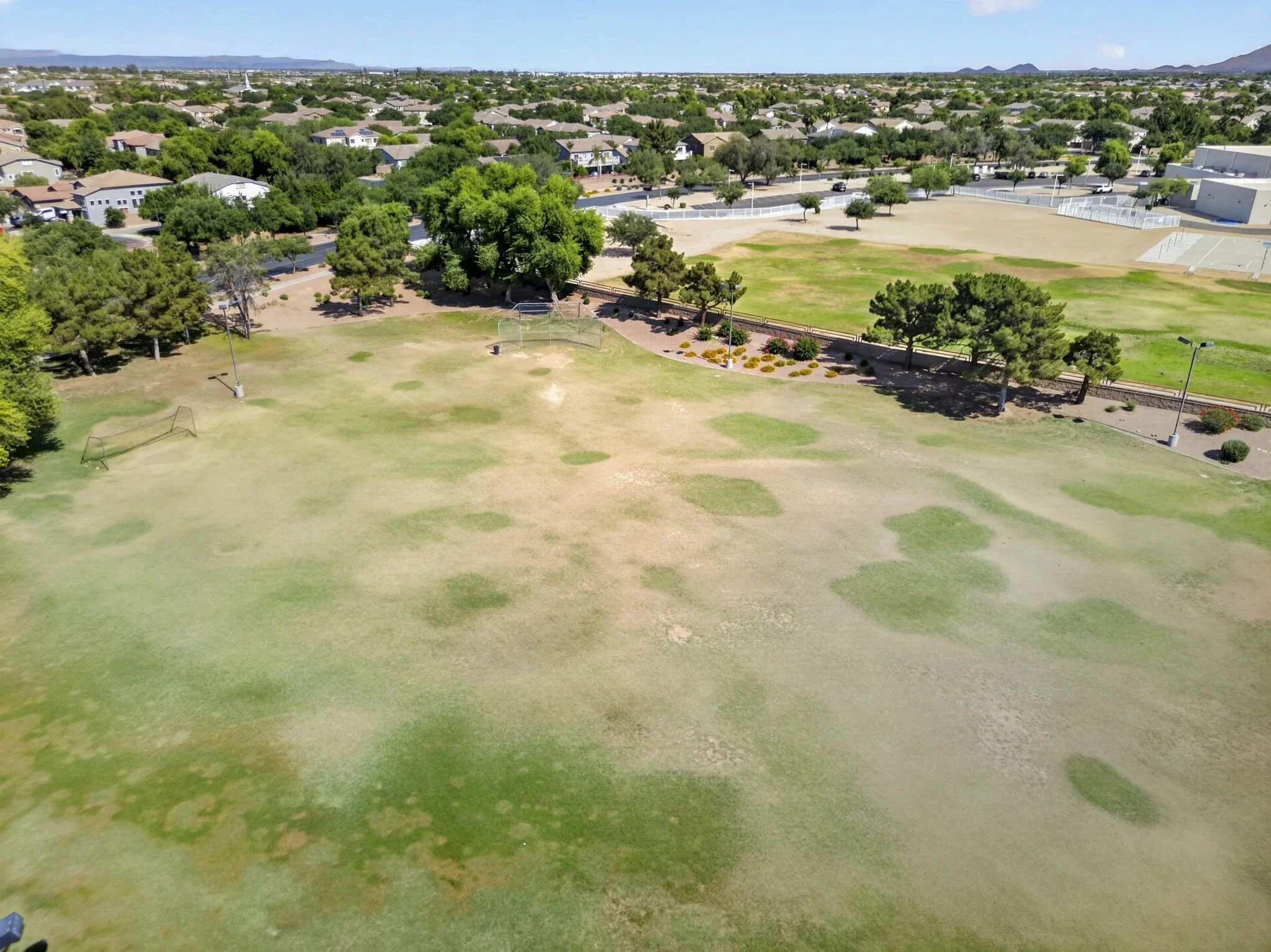 Aerial view of a park with green and brown grass areas, surrounded by a residential neighborhood with single-family homes and trees.