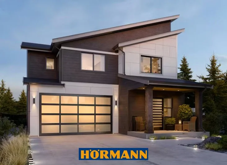 Modern two-story house with a garage, front porch, and outdoor seating area, surrounded by trees.