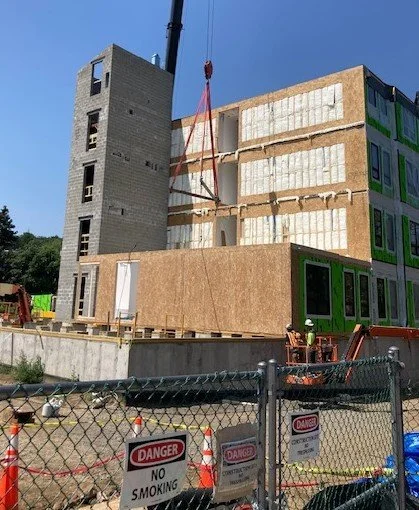 Construction site with an incomplete multi-story building, a tower crane lifting materials, and warning signs in the foreground.