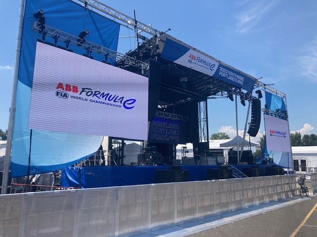 Empty stage setup for the ABB Formula E World Championship with large digital screens and sound equipment, outdoors under clear blue skies.