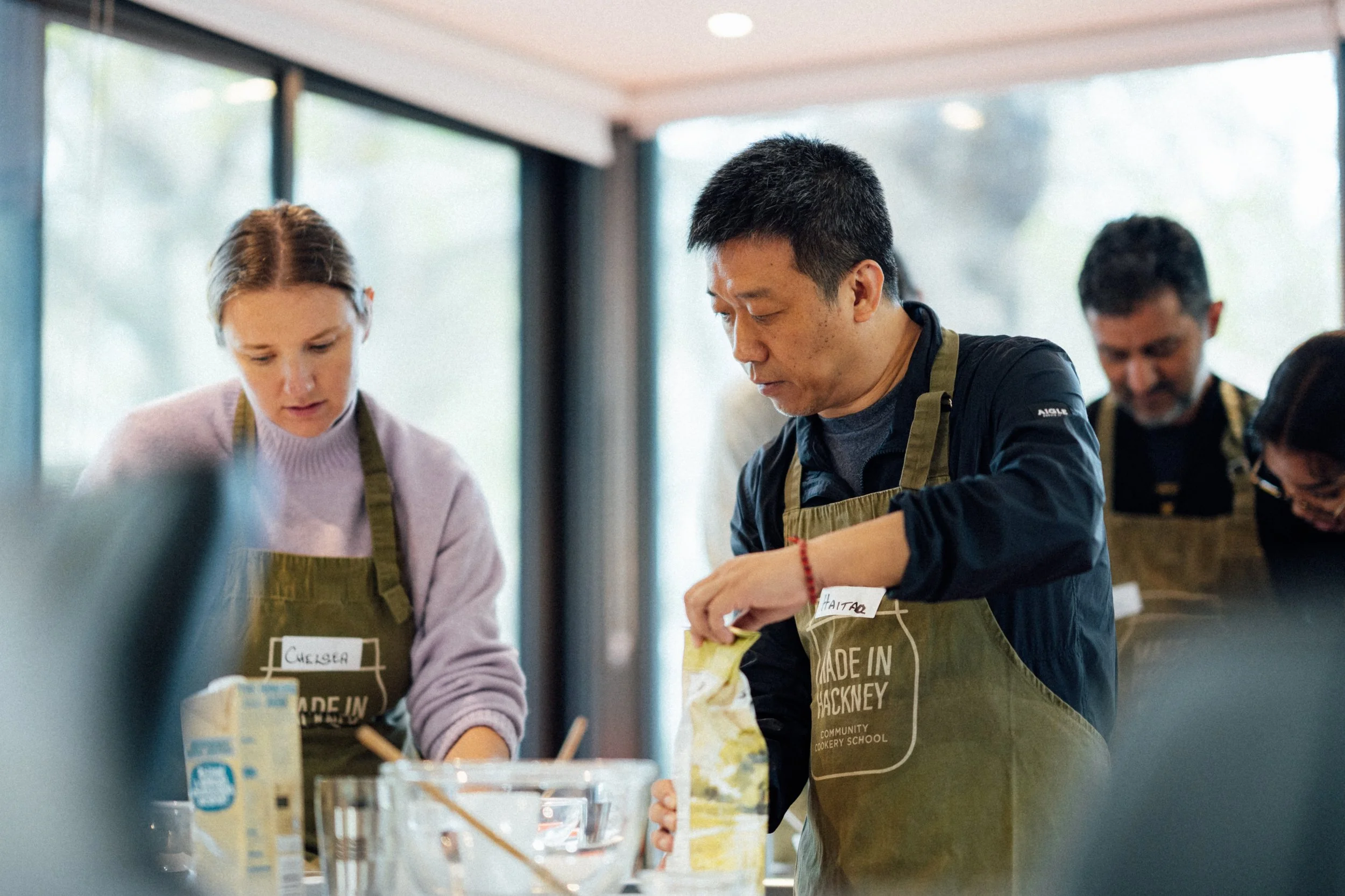 People baking and preparing ingredients in a kitchen classroom.