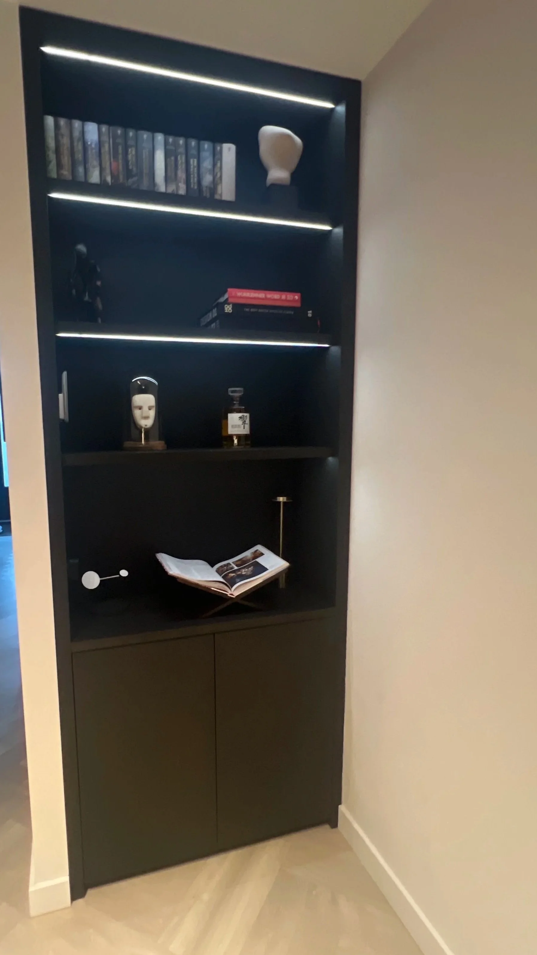 Een hoge, moderne boekenkast of kast met meerdere planken en ingebouwde LED-verlichting, geplaatst in een hoek van een kamer.