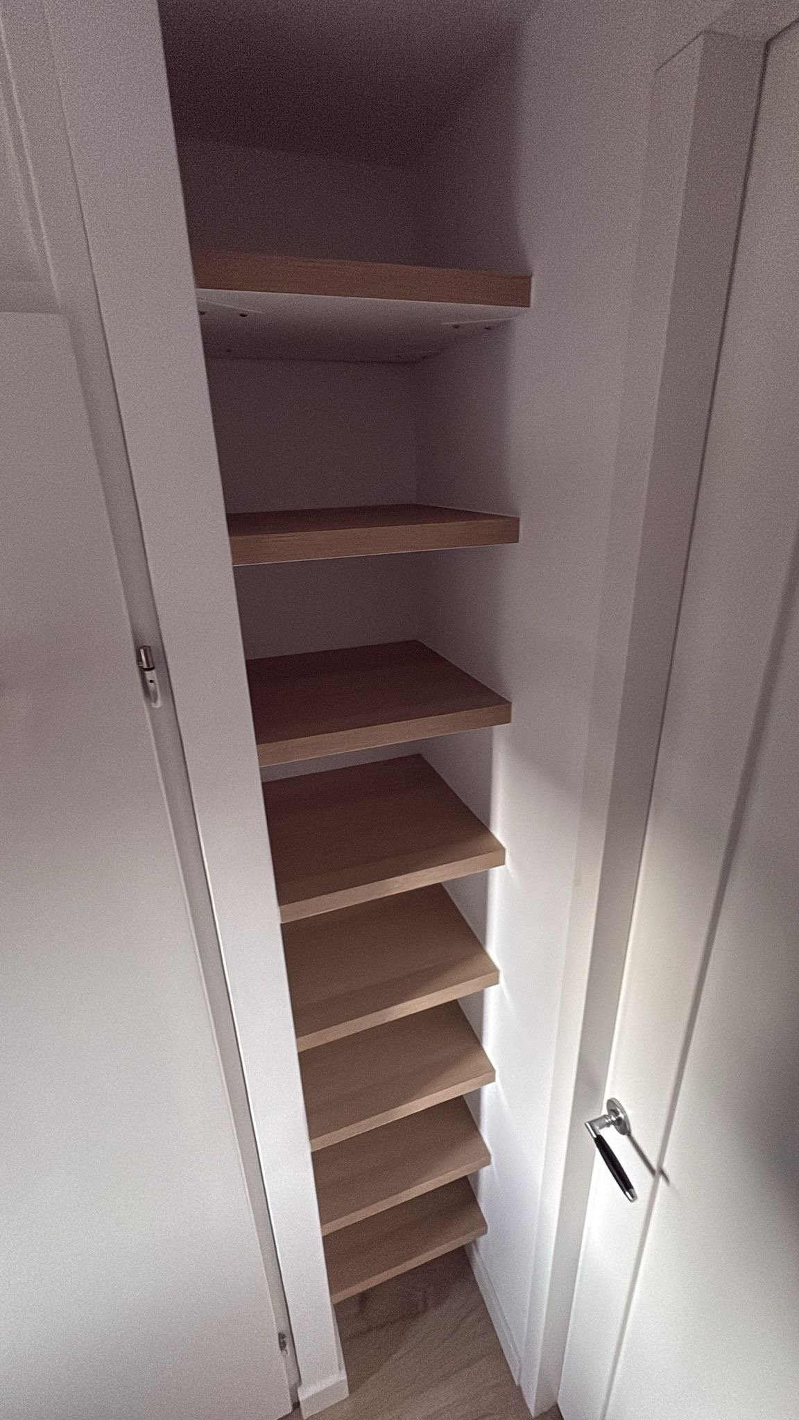 Een lege witgekaleide schoenenkast met meerdere houten planken.