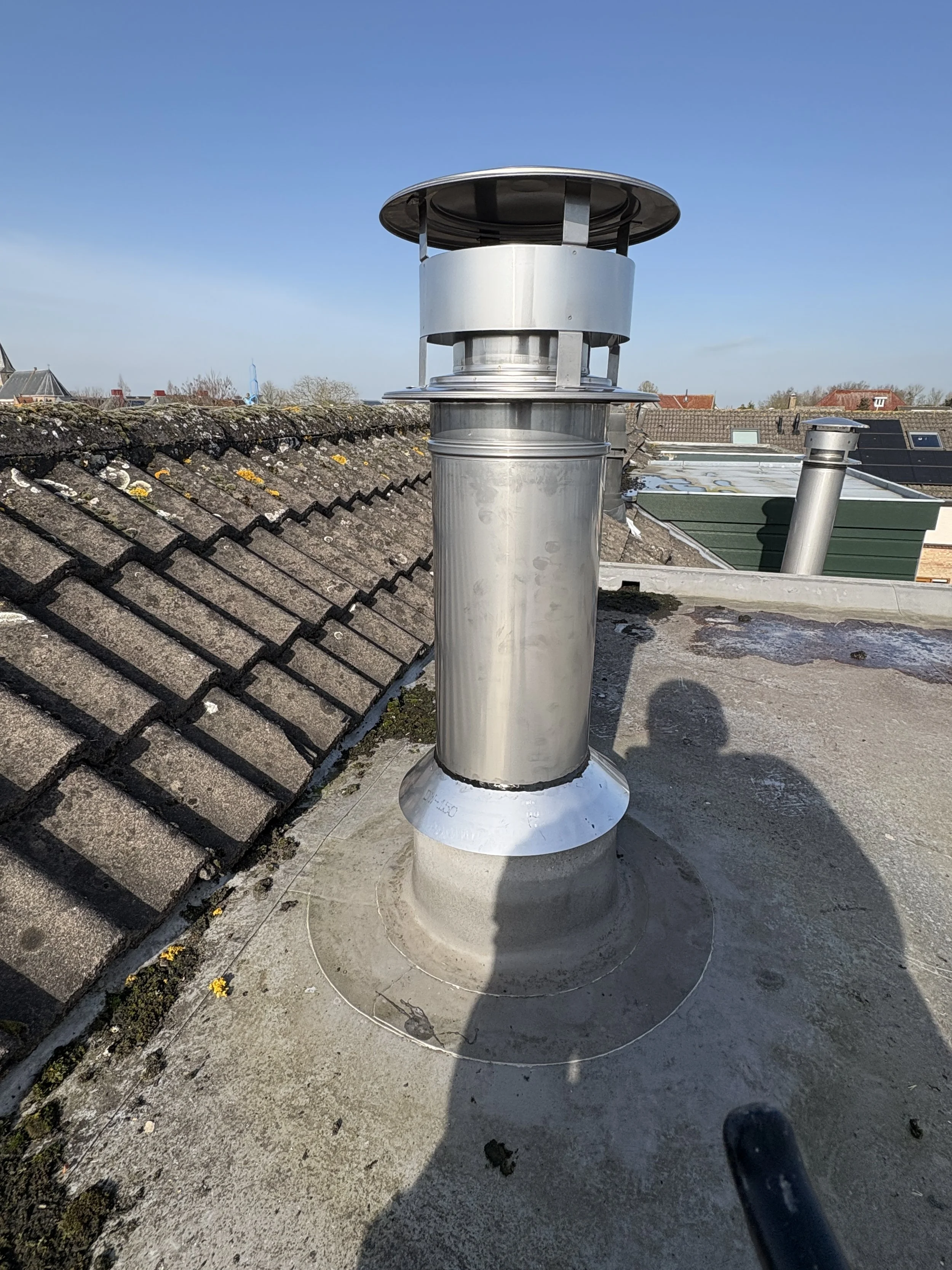 Metalen ventilatiepijp op een dak onder een blauwe hemel.