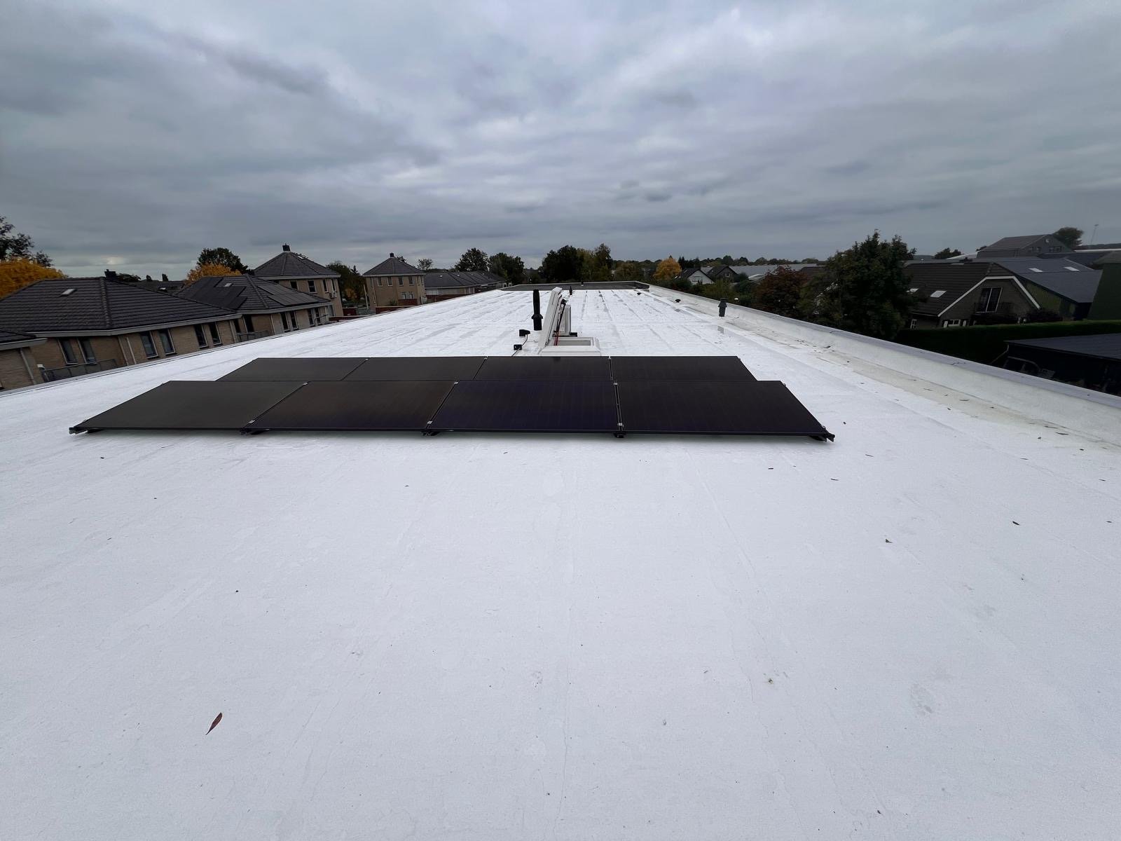 Zwarte zonnepanelen op een wit plat dak onder een bewolkte hemel.