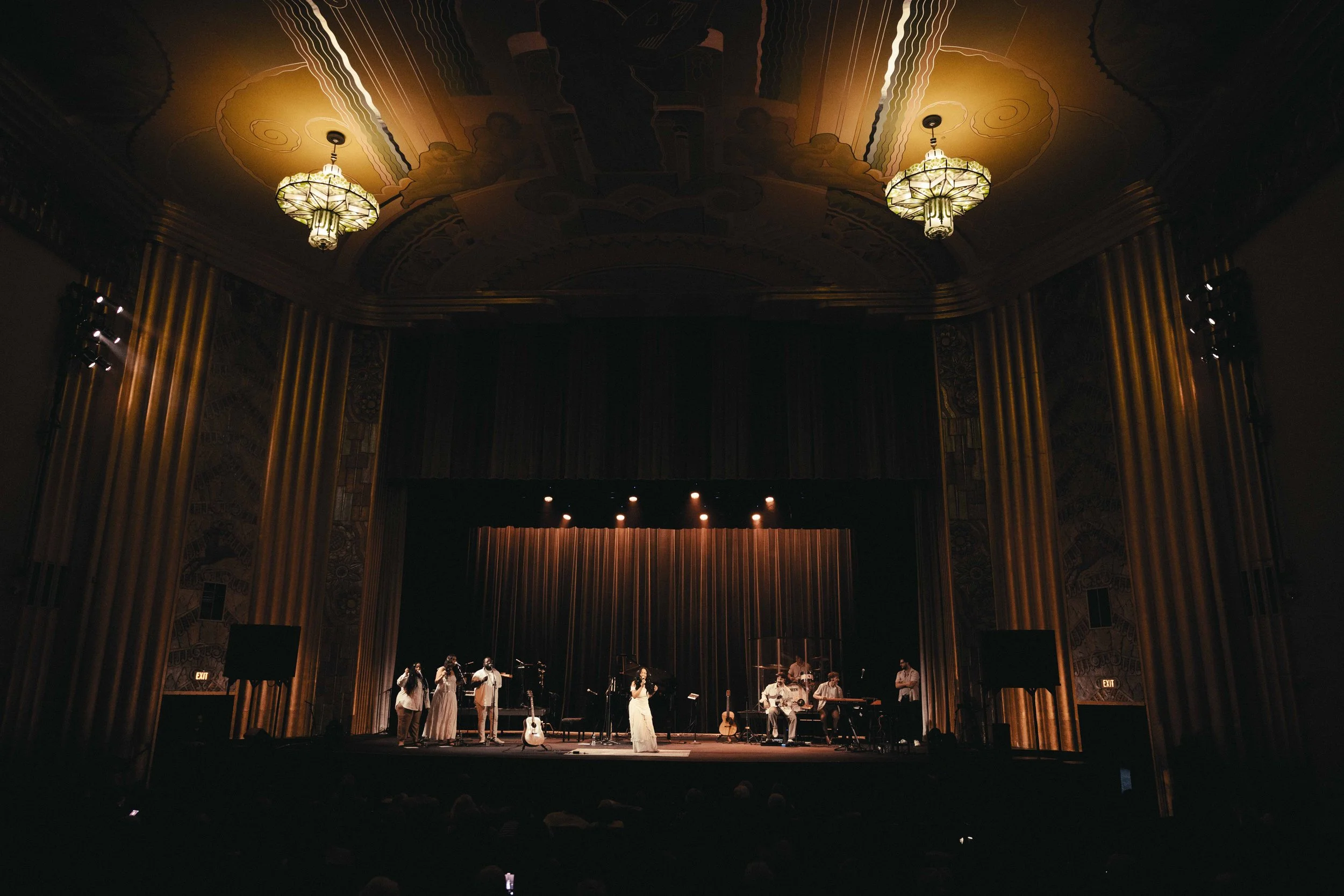 A musical performance on stage in a theater with ornate ceiling and lighting fixtures.