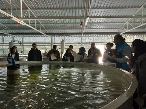 People gathered around a circular fish tank inside a fish farm.