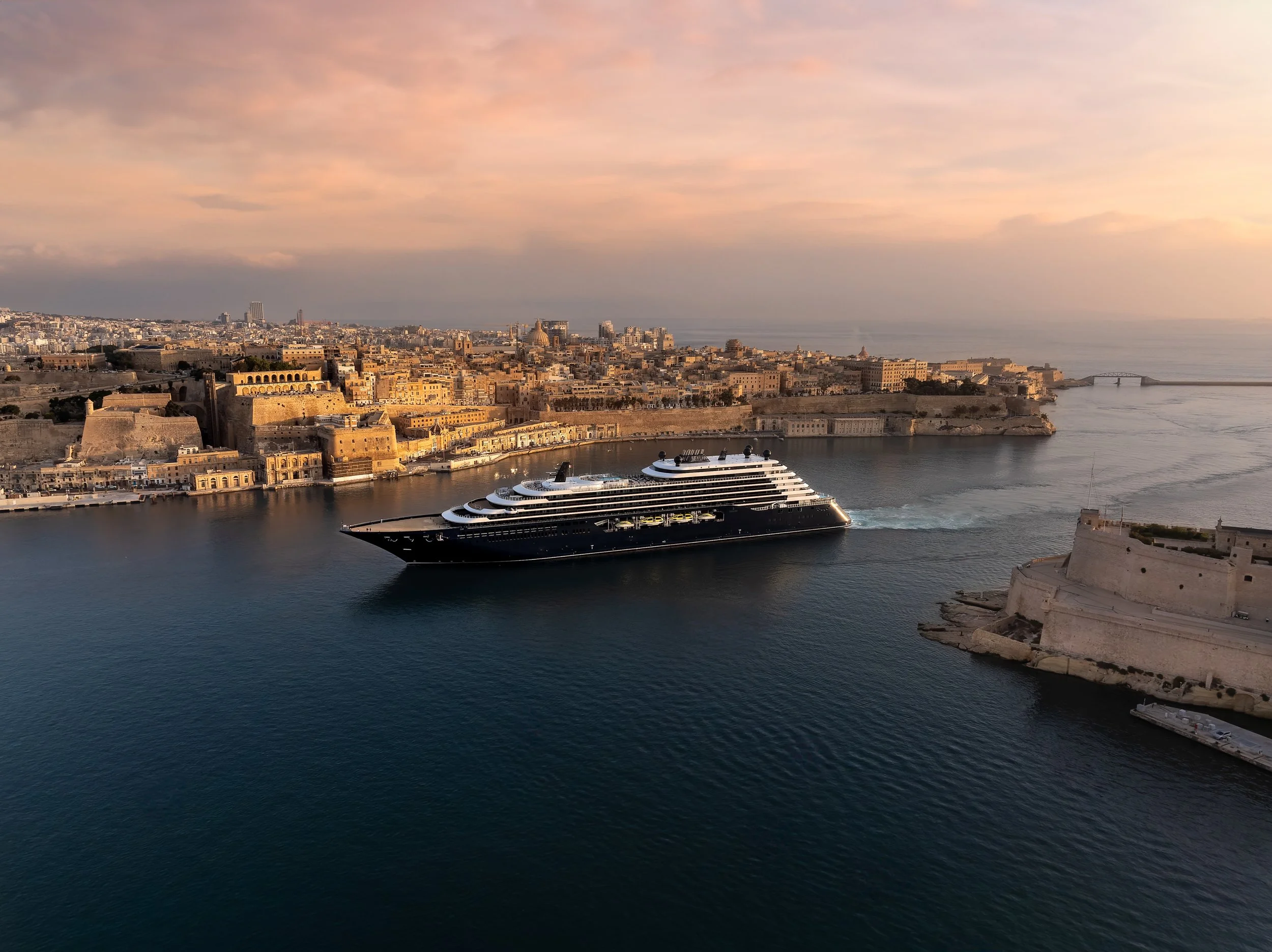 The Ritz-Carlton Yacht Collection superyacht Ilma sailing from a Mediterranean port at sunset.