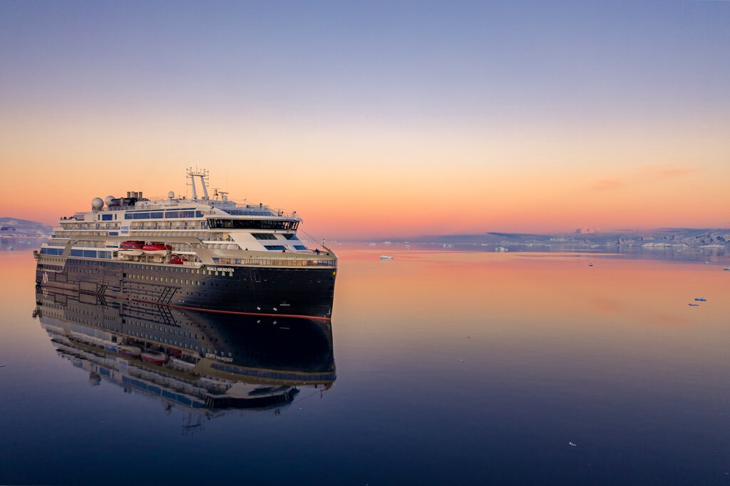 An HX expedition ship at anchor in calm polar waters at sunset, surrounded by ice.
