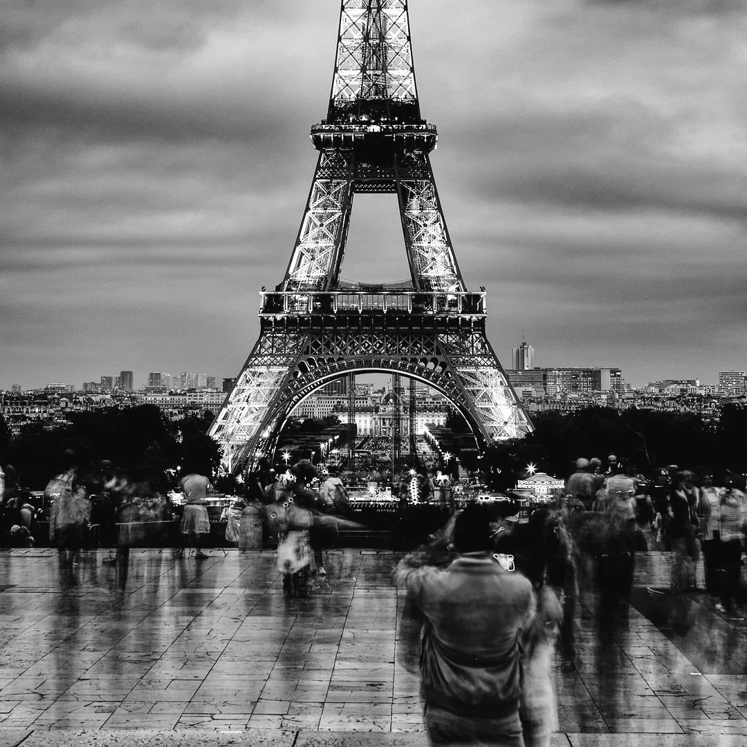 Long‑exposure HDR black‑and‑white photograph of the Eiffel Tower seen from Trocadéro, with blurred crowds in the foreground and illuminated architecture behind.
