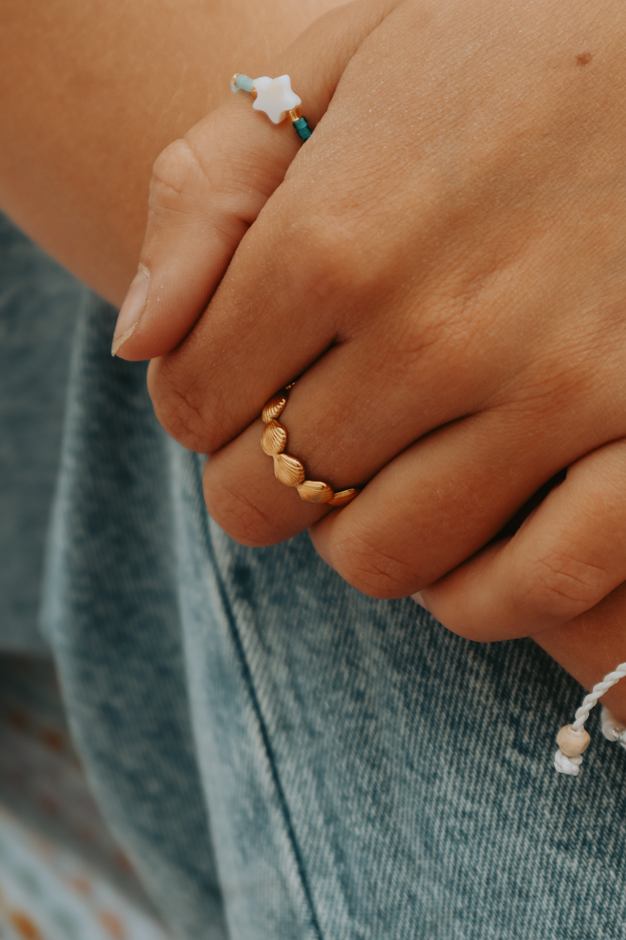 Close-up of a hand with a gold ring wearing a beaded bracelet, holding the collar of a garment made of blue denim fabric.