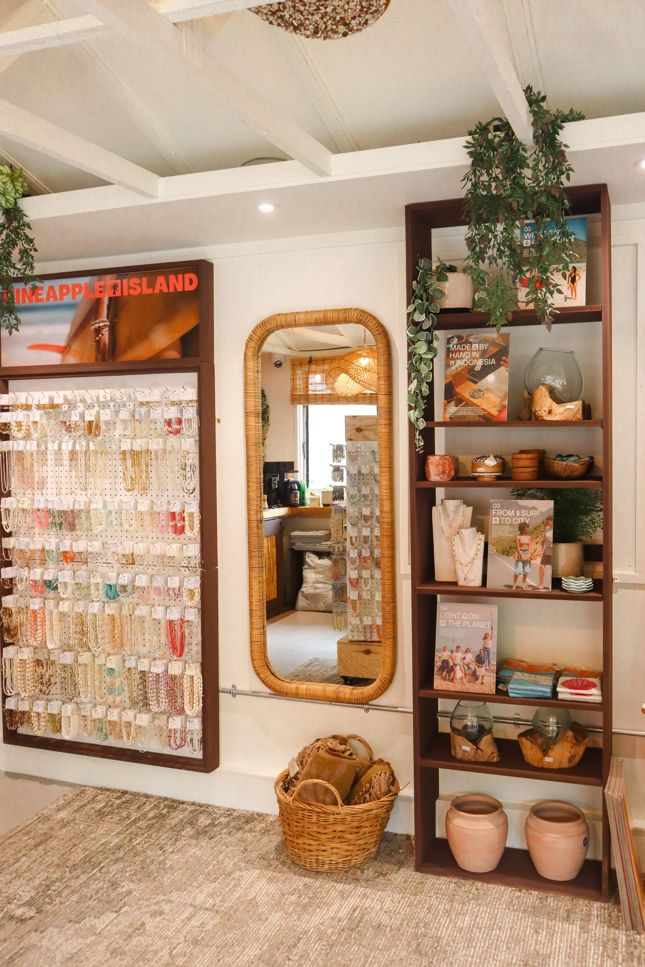 Interior of a store with jewelry, pottery, and decorative items on wooden shelves and displays, along with a large mirror and hanging plants. Pineapple Island Jewellery Photography