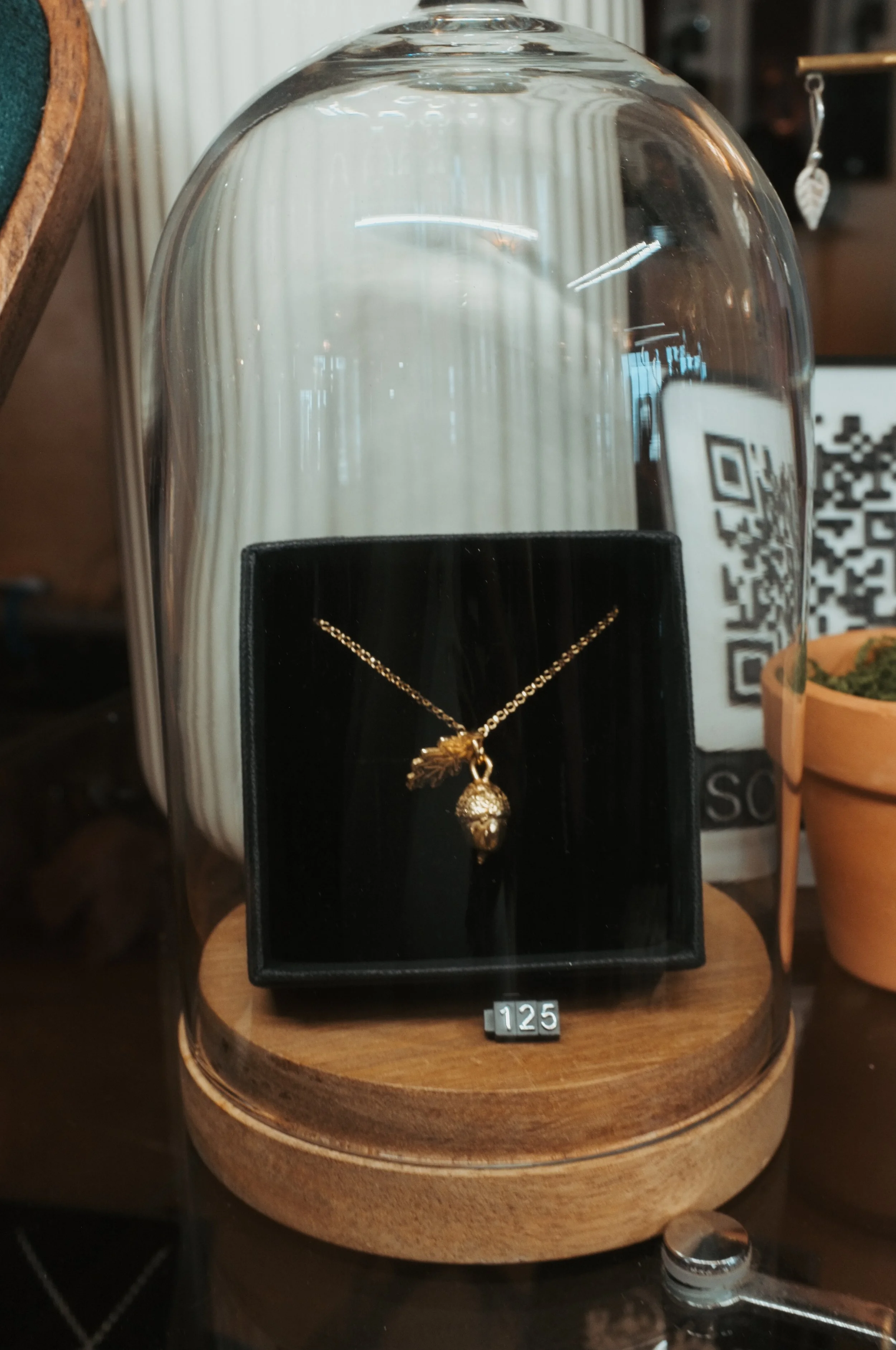 Gold necklace with a pendant displayed inside a glass dome on a wooden base.