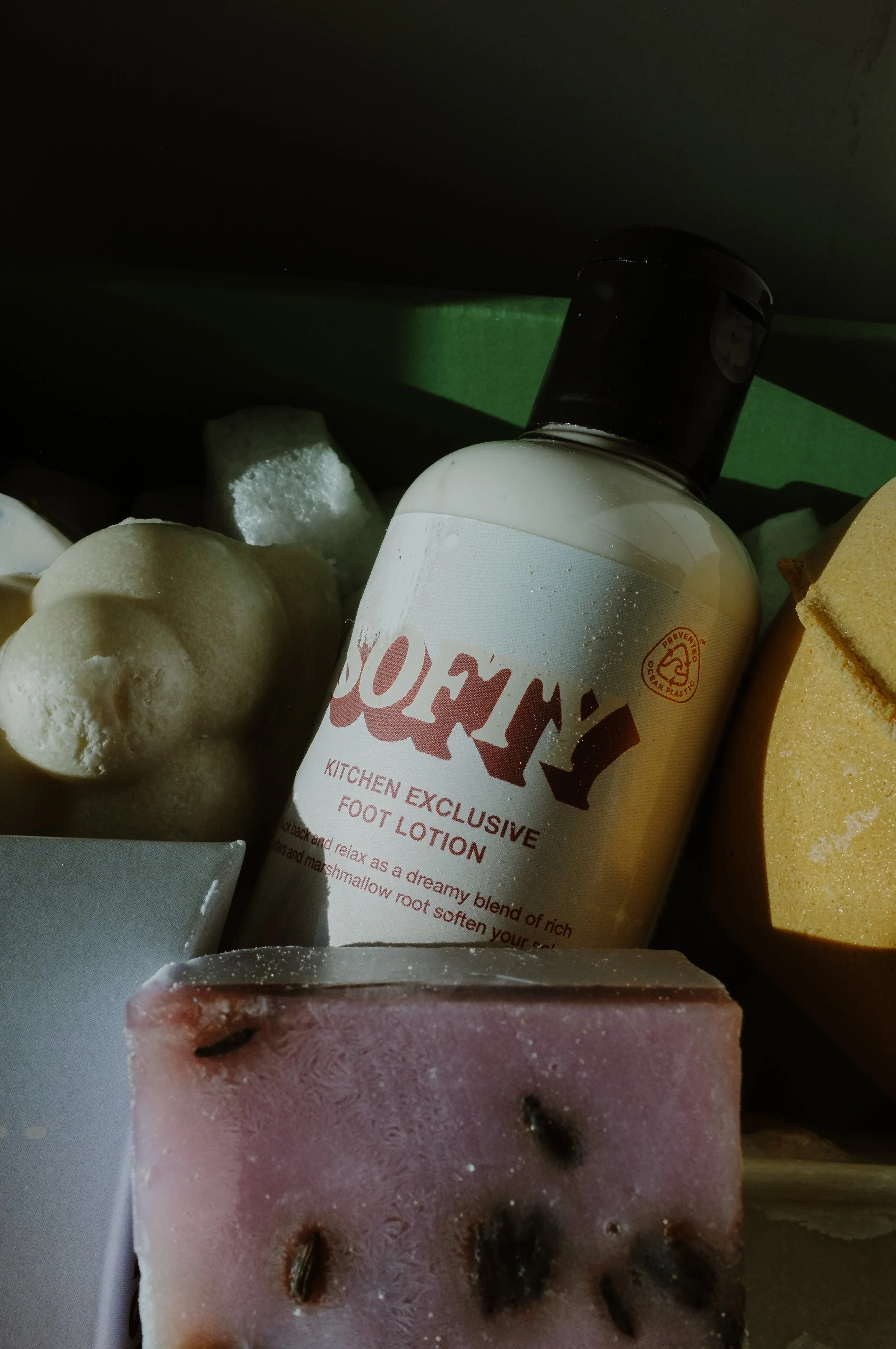 A bottle of SOCKY kitchen exclusive foot lotion surrounded by soap bars and bath bombs.