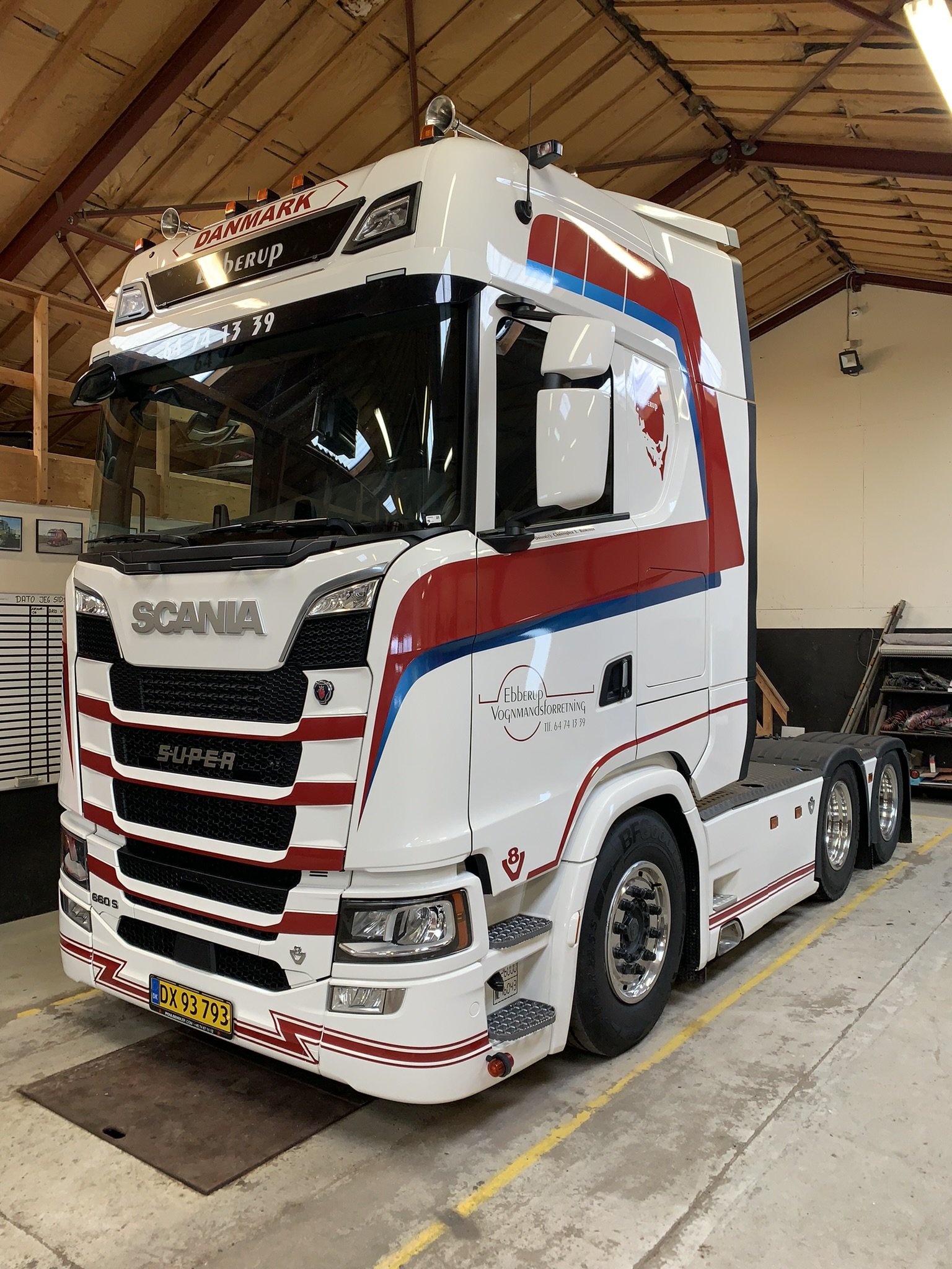 En stor hvid lastbil med rød og blå grafik, parket indendørs i en garage-lignende bygning.
