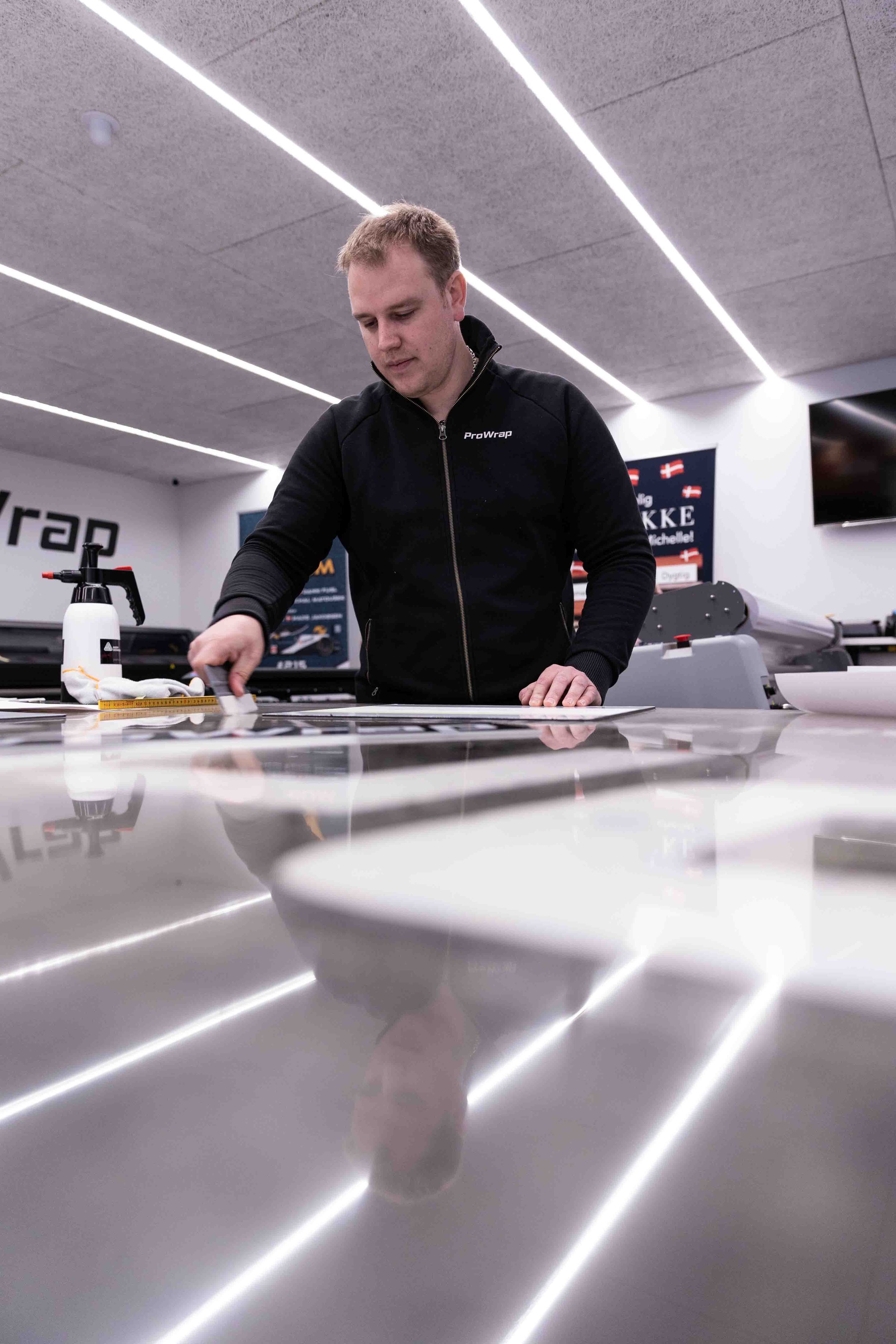 En mand arbejder i et moderne lufttændt rum med glatte hvide bordoverflader, der har reflekterende overflader og LED-stripbelysning i loftet.
