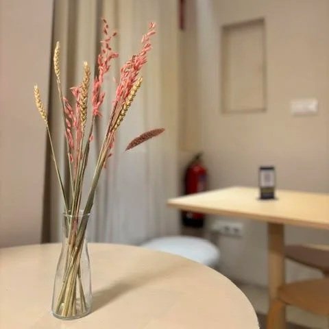 Decoración minimalista en Perrisimo Dog Café: jarrón de cristal con flores secas y pampas en tonos rosa y beige sobre mesa blanca, creando un ambiente nórdico y acogedor.