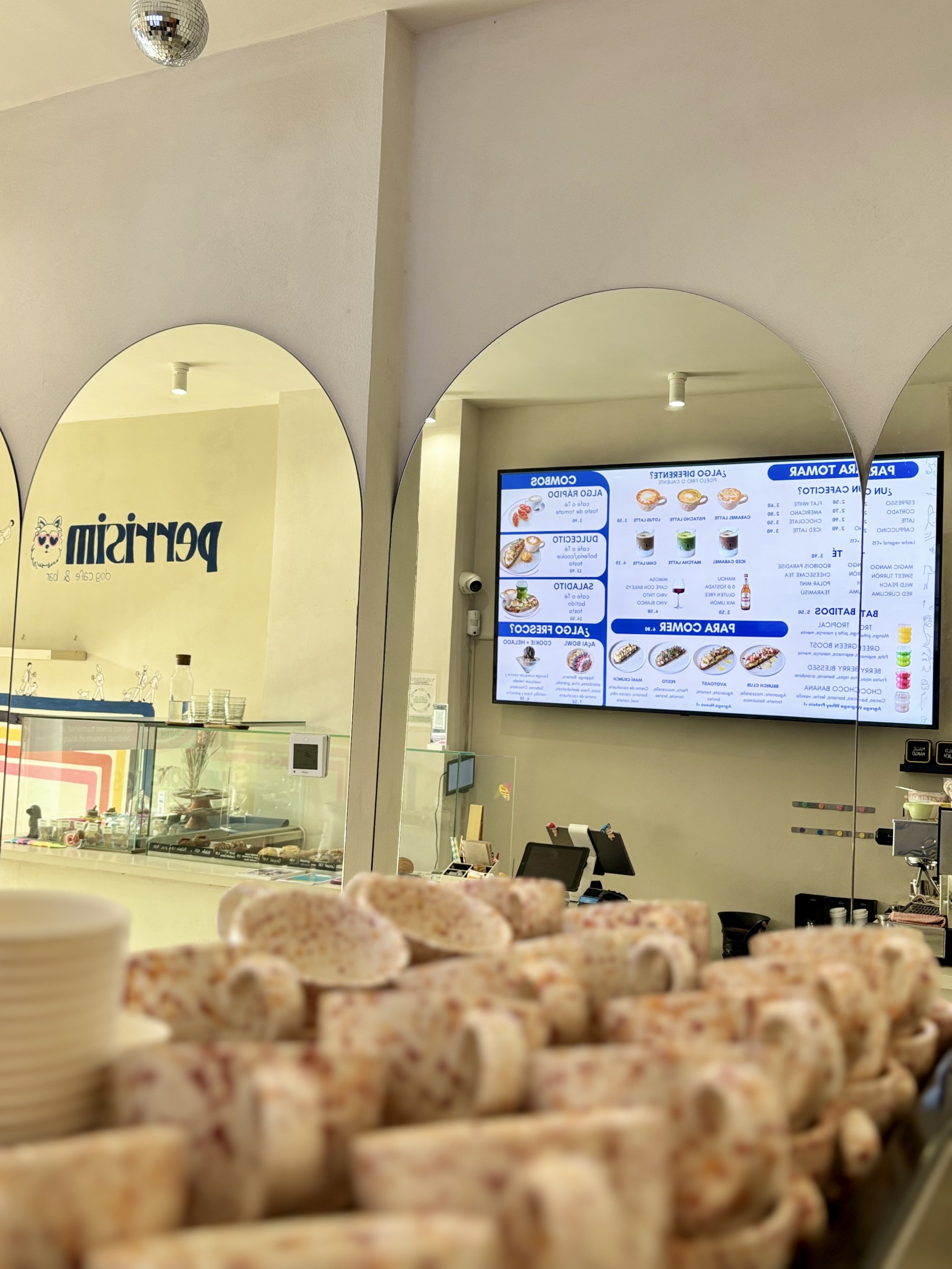 Interior moderno de Perrisimo Dog Café en Madrid con espejos en arco, barra de café de especialidad y carta digital con opciones para perros y humanos.