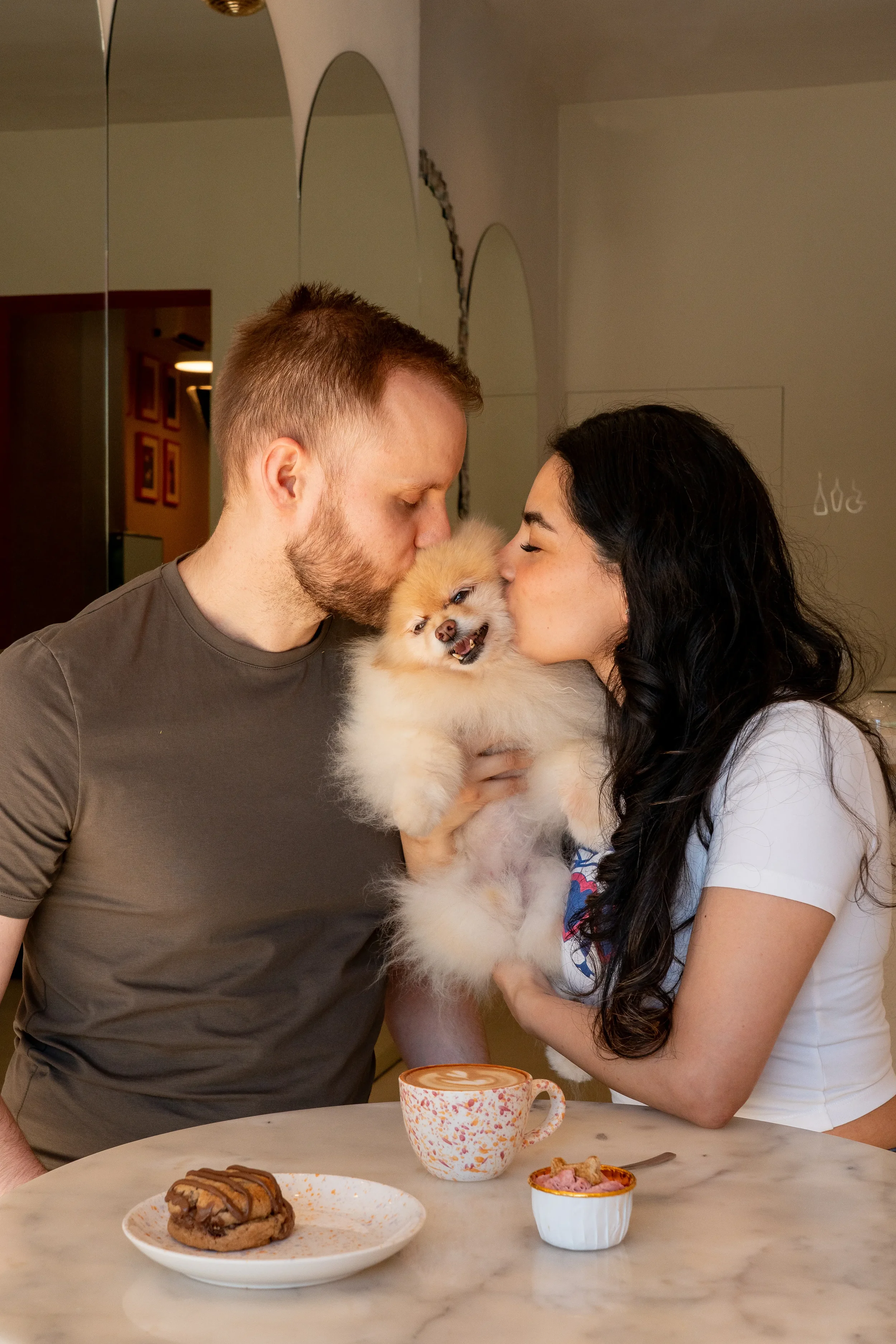 Pareja besando a su pomerania mientras toman un café en Perrísimo, la cafetería pet-friendly donde ir con tu perro en el barrio de Retiro, Madrid