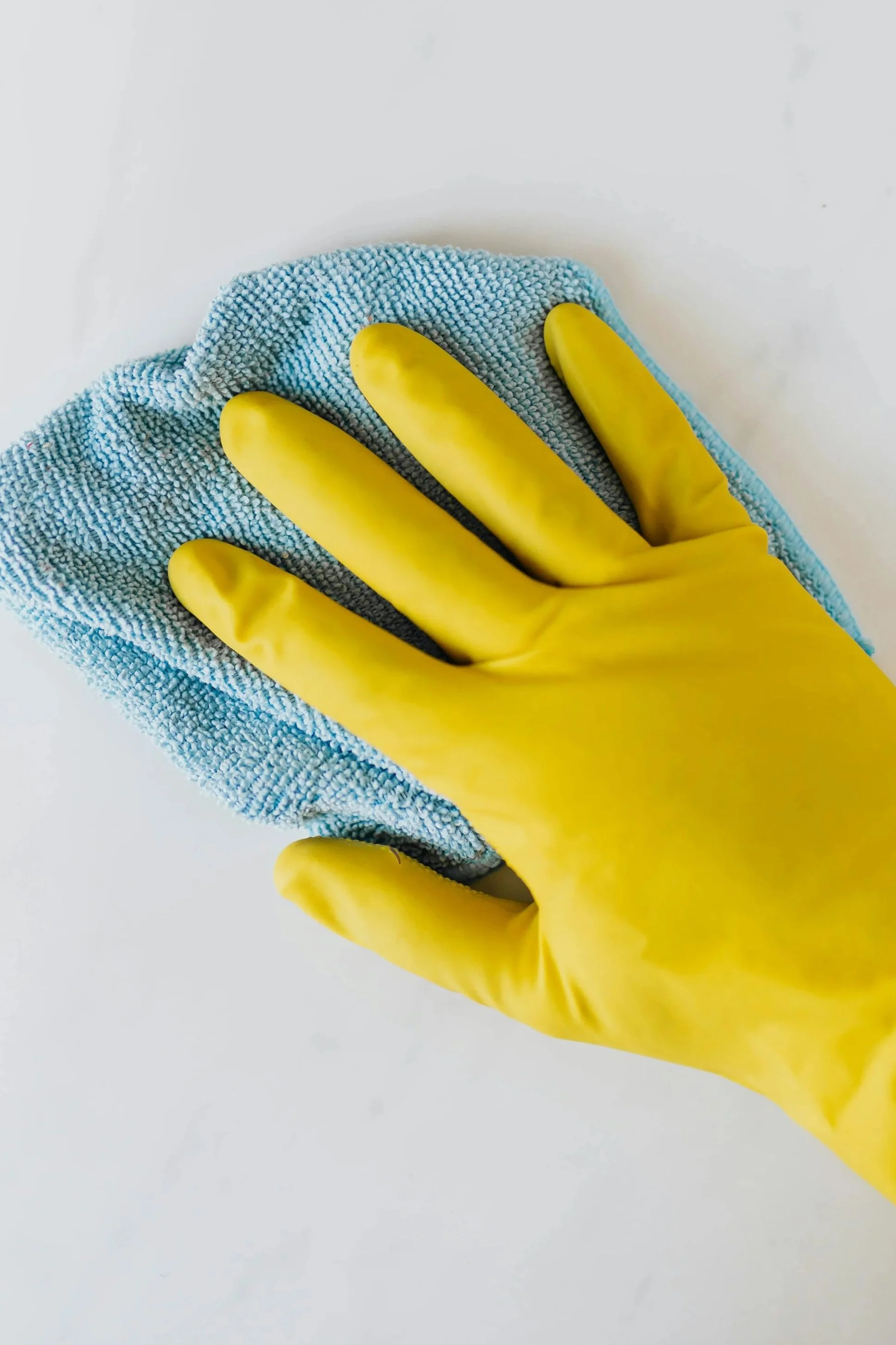 A gloved hand cleaning a white surface with a blue microfiber cloth.