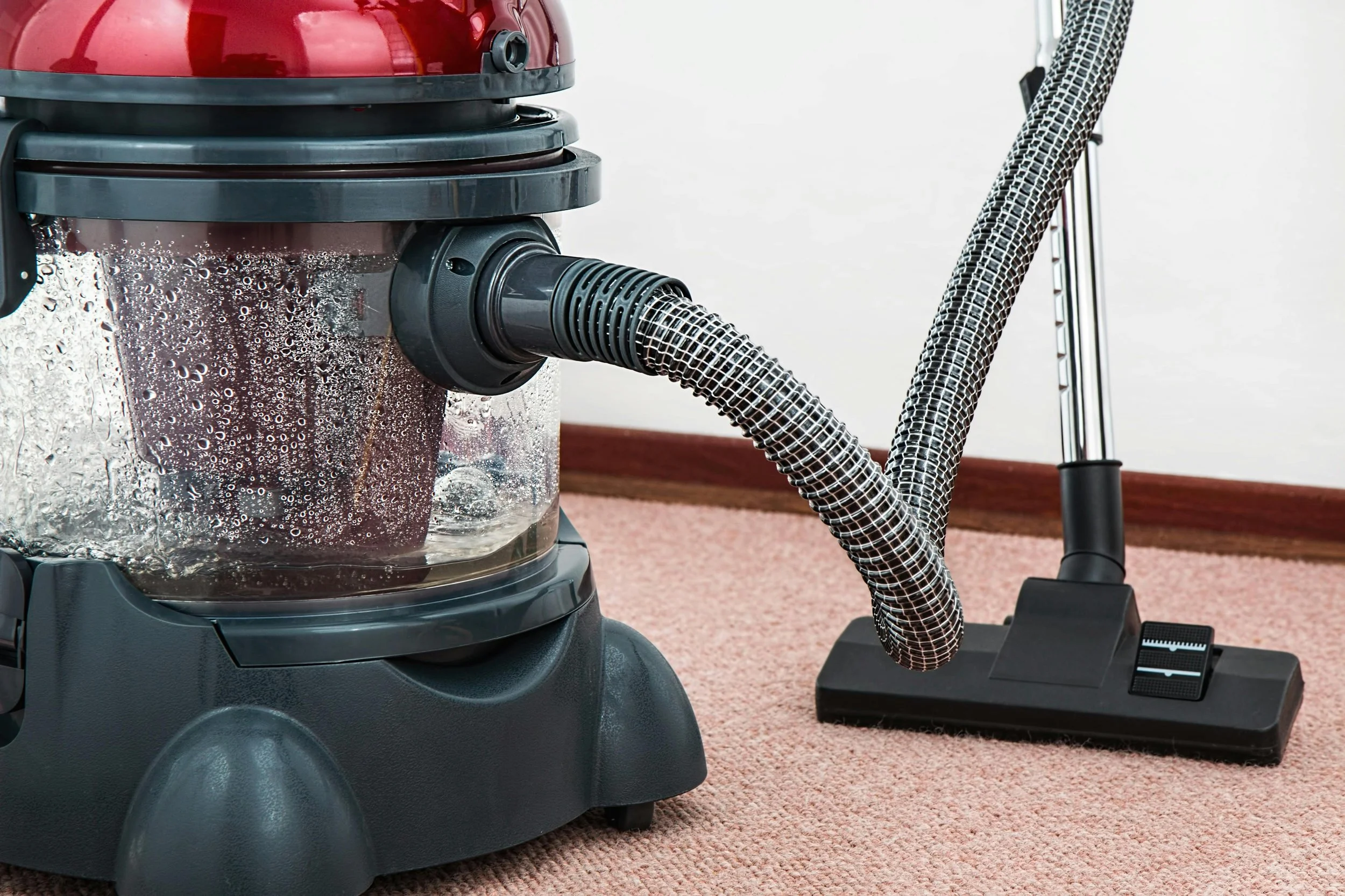 A vacuum cleaner with a transparent dust container on a carpeted floor.