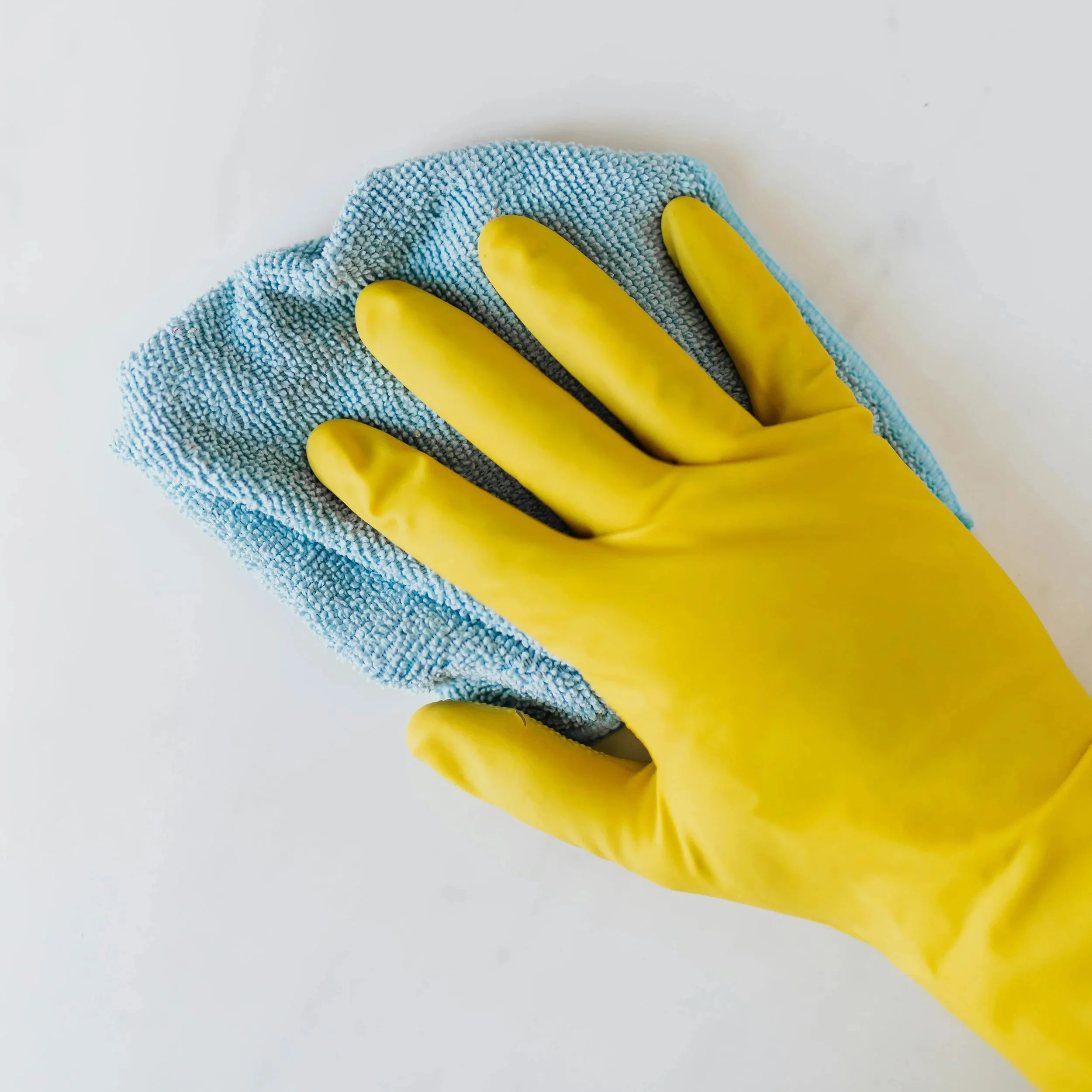 A hand wearing a yellow rubber glove wiping a white surface with a blue cloth.