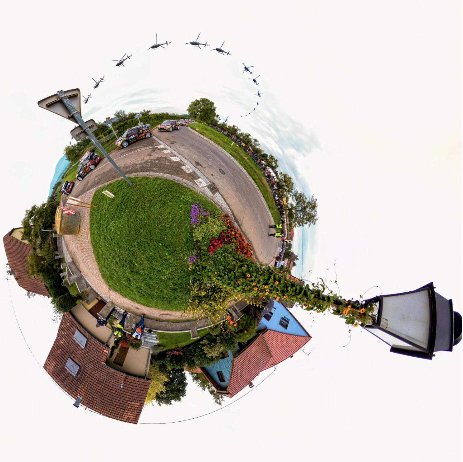 Stereographic projection of a street scene with houses, cars, and a flower garden, surrounded by a sky with flying helicopters.