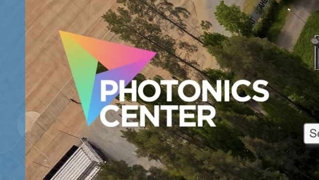 Logo of the Photonics Center with a triangular multicolored symbol, overlaid on an aerial view of a forested area.