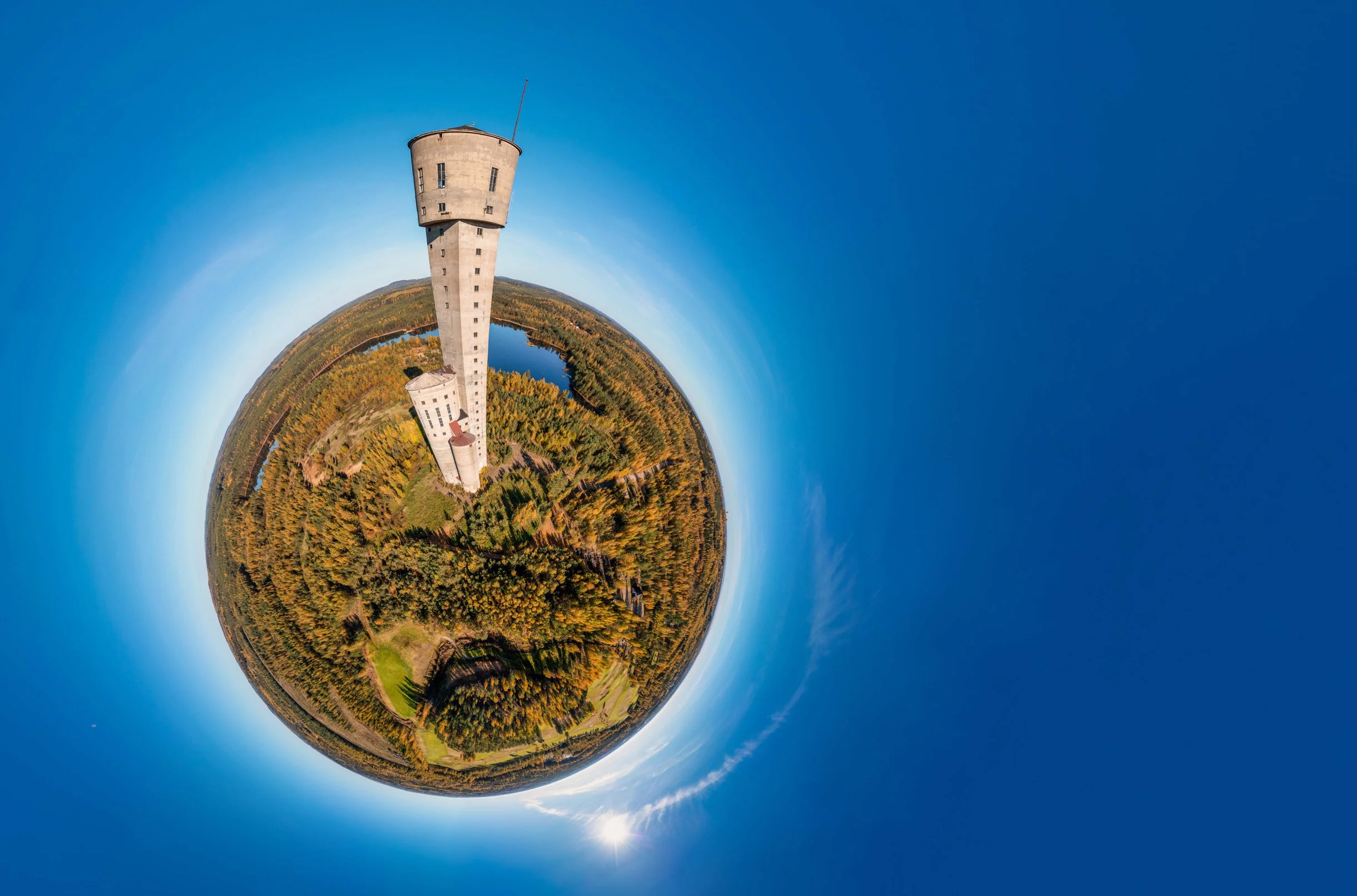 360-degree aerial view of a tall tower surrounded by forested landscape and a clear blue sky, resembling a small planet.