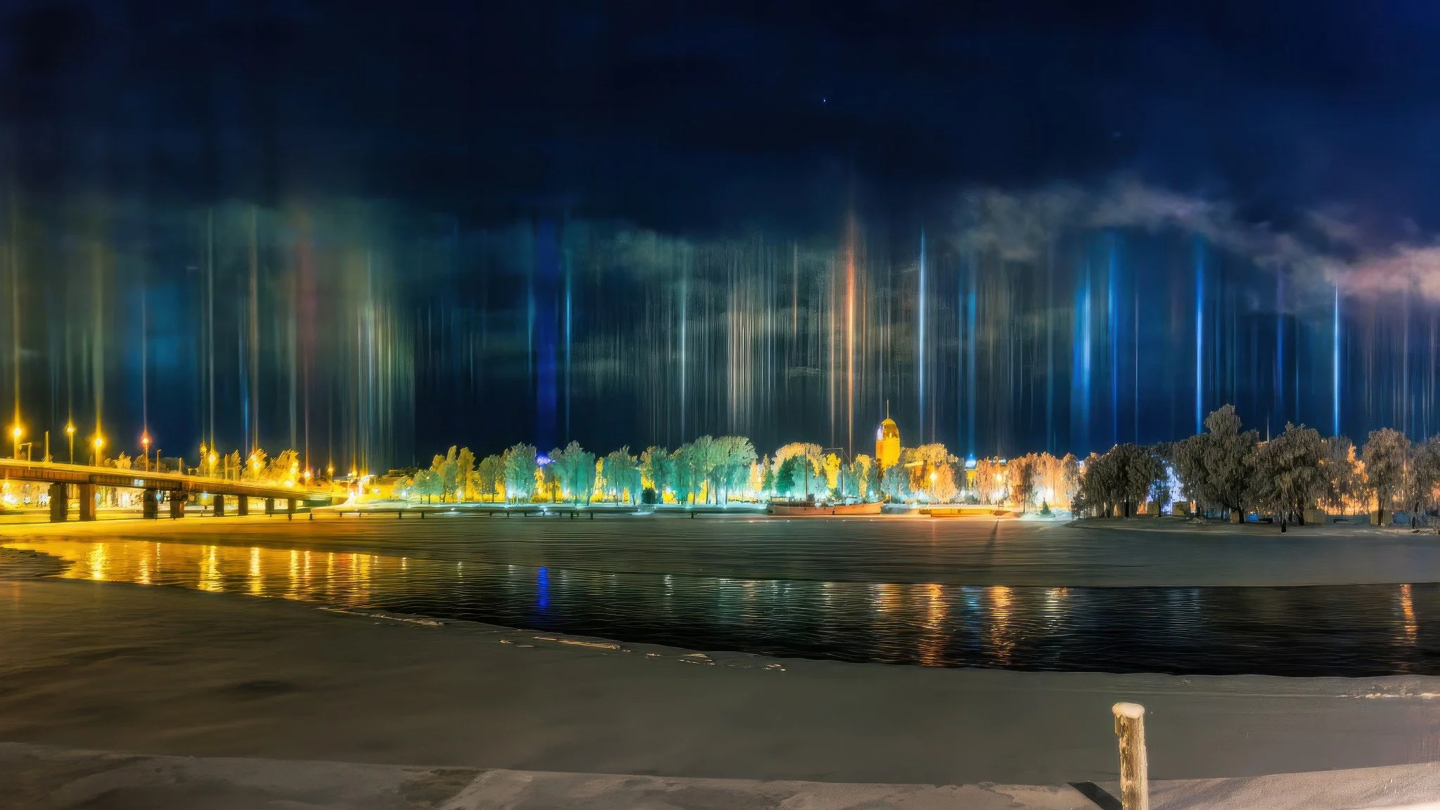 Nighttime street scene with colorful vertical light beams reflecting on water, illuminated trees, a bridge on the left, and a church with a dome in the distance.