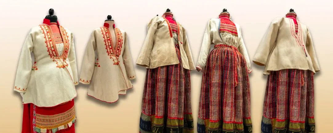 Traditional Eastern European folk costumes displayed on mannequins, featuring embroidered blouses, patterned skirts, and decorative aprons.