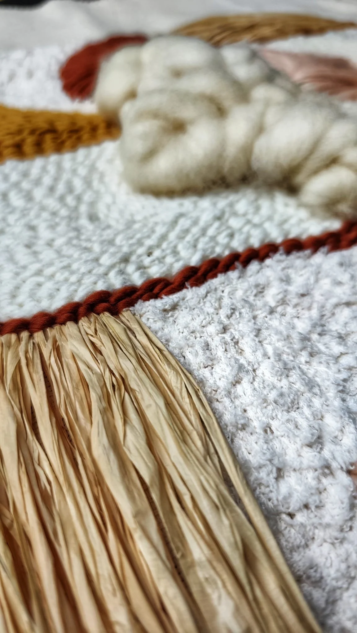 Close-up of a decorative woven and fringed trim on a textured fabric surface.