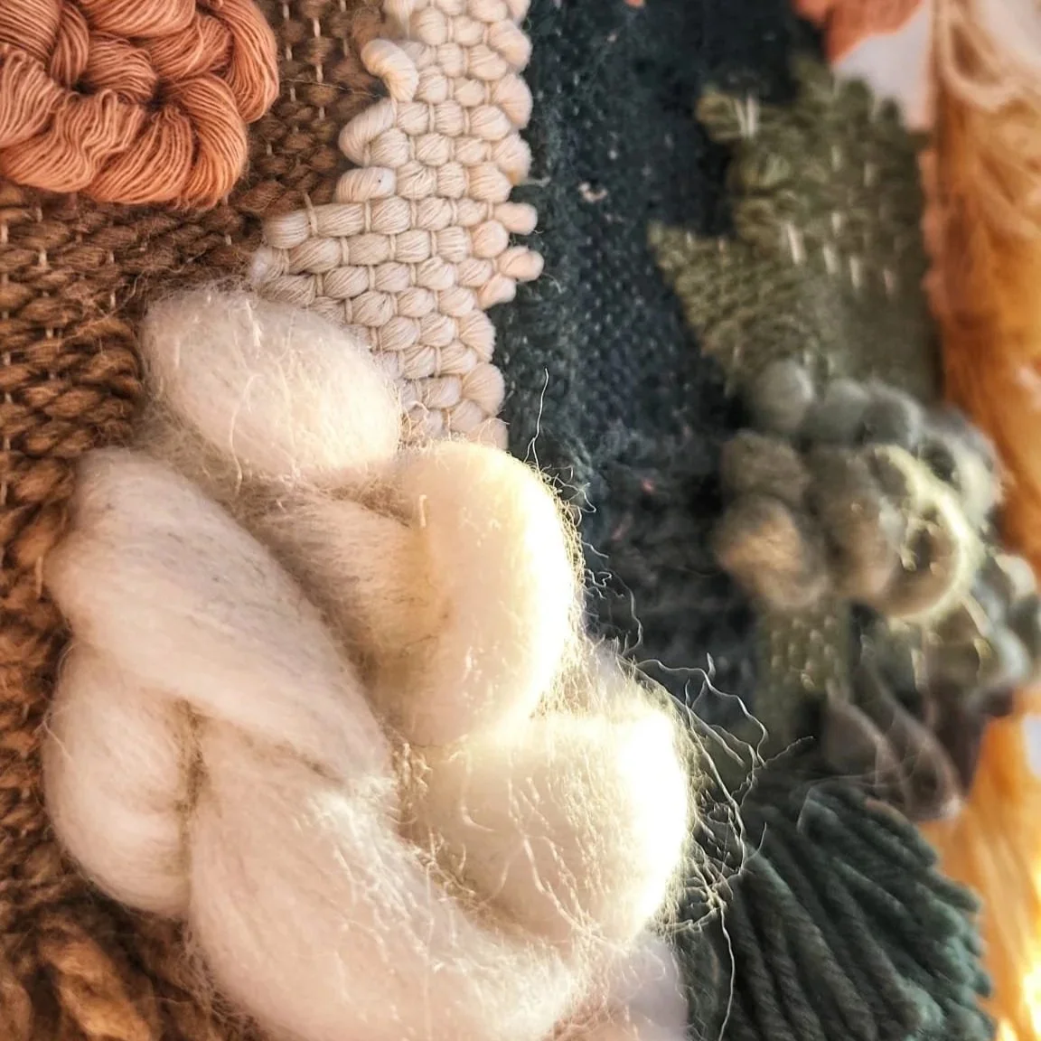 Close-up view of various roving wool fibers in shades of cream, black, and brown, arranged on a textured woven fabric background.