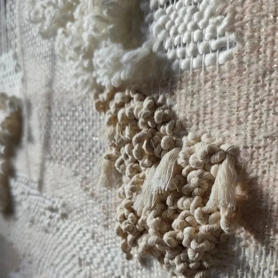 Close-up of white yarn bundles and woven textile on a textured surface.