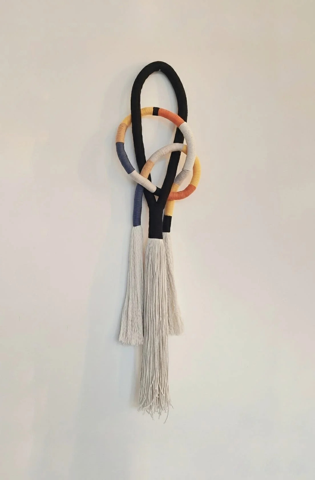 Decorative wall hanging using wrapping technique in various colors against a plain wall. Macrame.