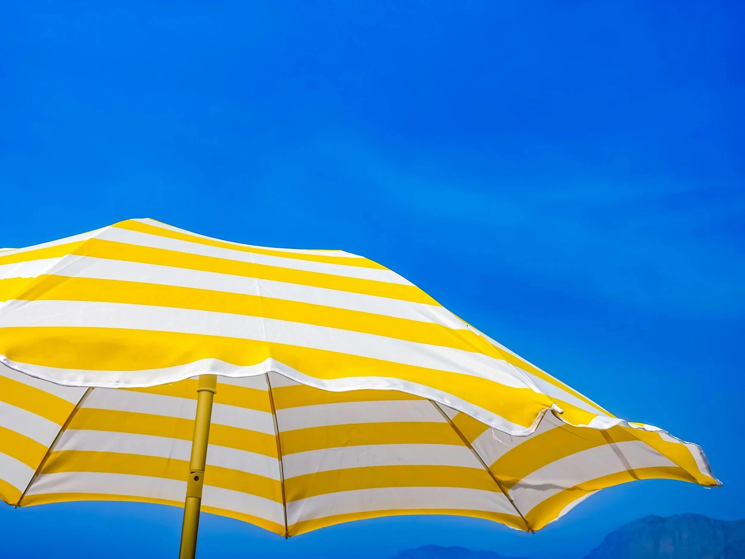 Yellow and white striped beach umbrella against a bright blue sky.