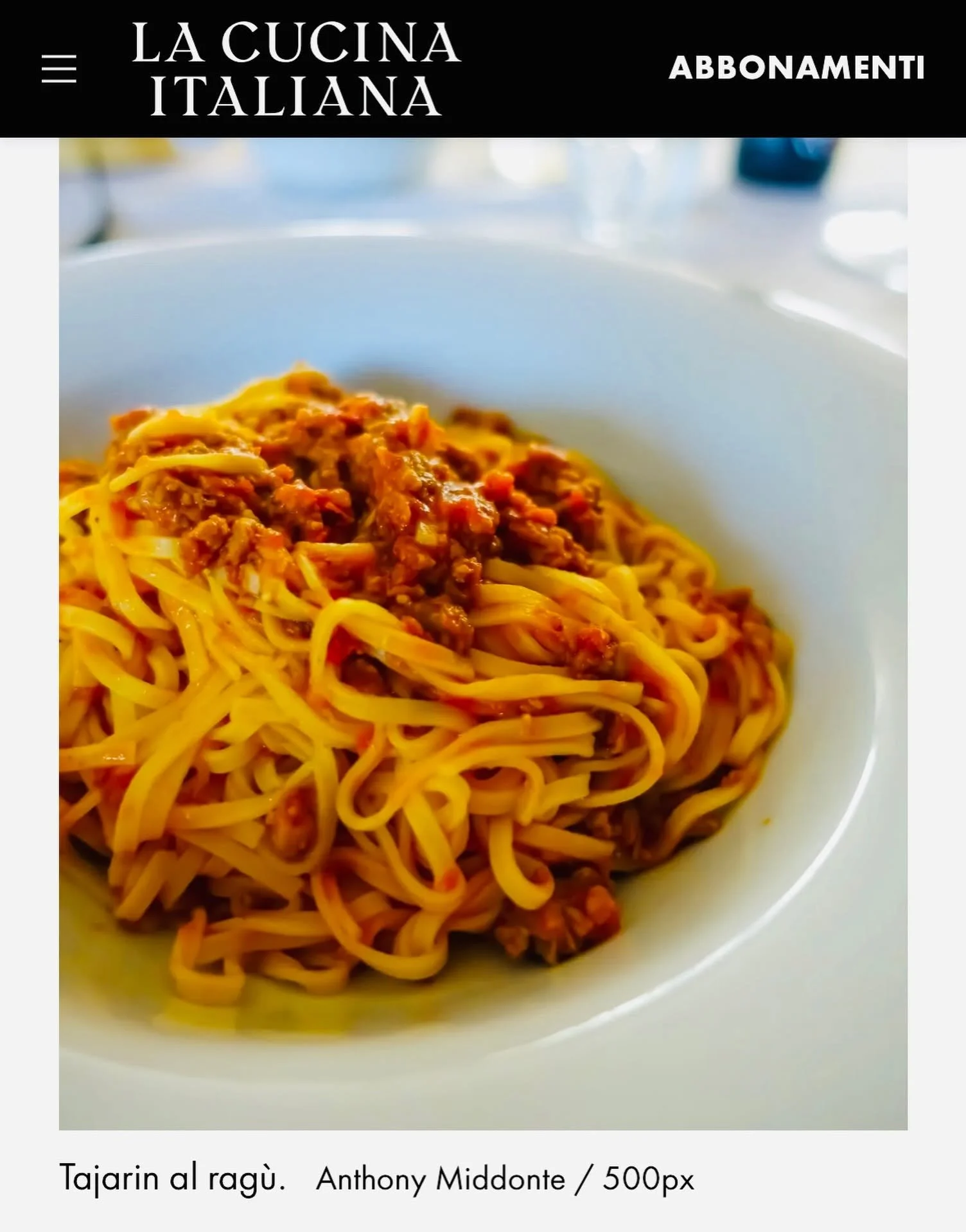 A bowl of spaghetti with ragù sauce on top, photographed on a white surface.