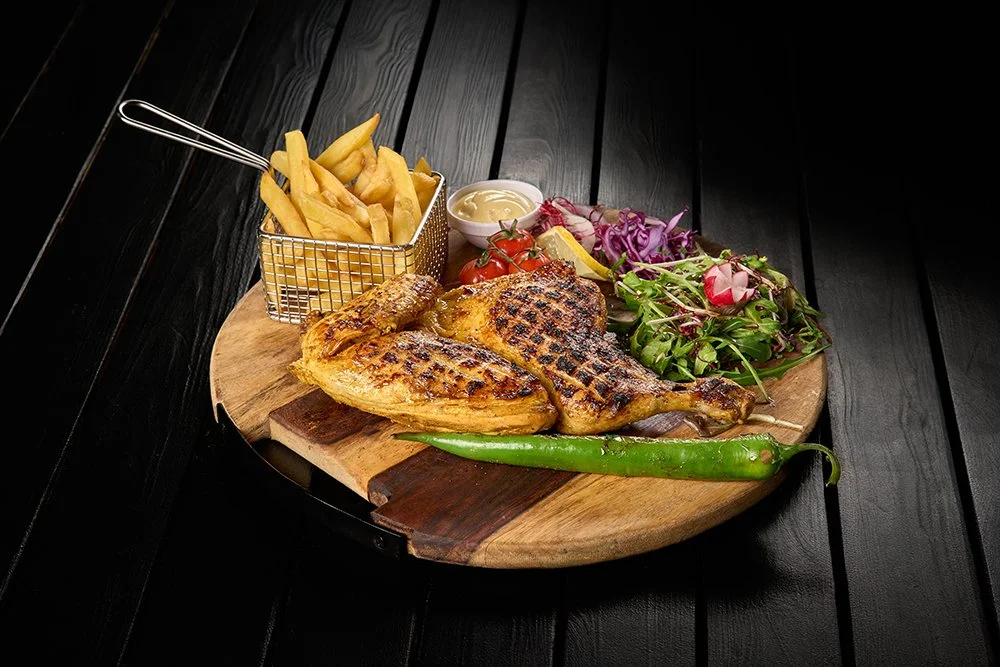 Geroosterde kip, friet, salade met radijsjes, tomaten, ui en een groene peper op een houten serveerschaal.