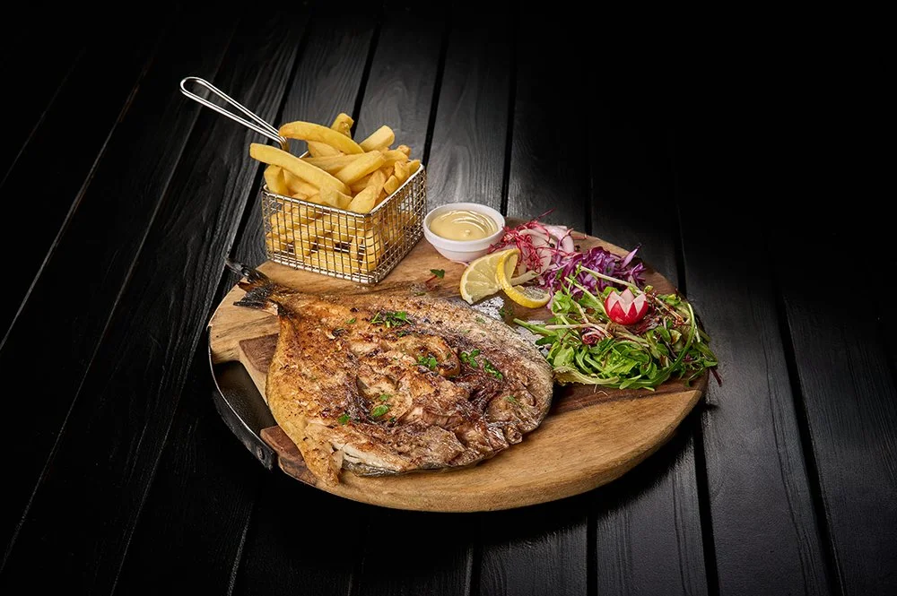 Gegrilde vis met frietjes, salade en saus op een houten bord