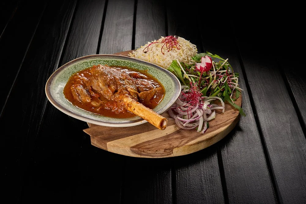 Een bord met curry, rijst en salade op een houten snijplank op een zwarte tafel.