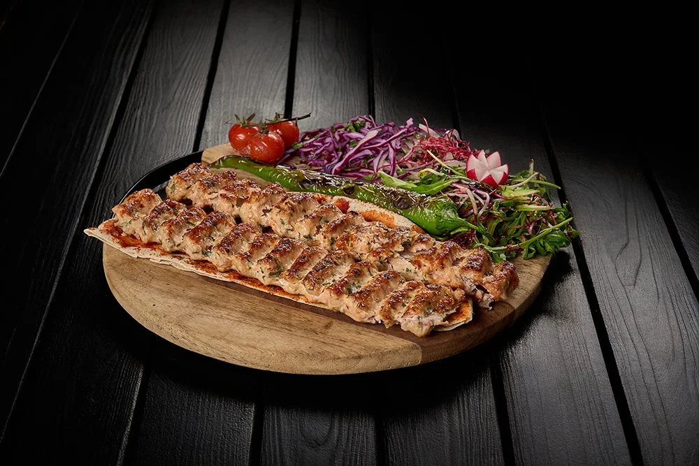 Gegrilde kip rollade met salade en tomaatjes op een houten serveerschaal.