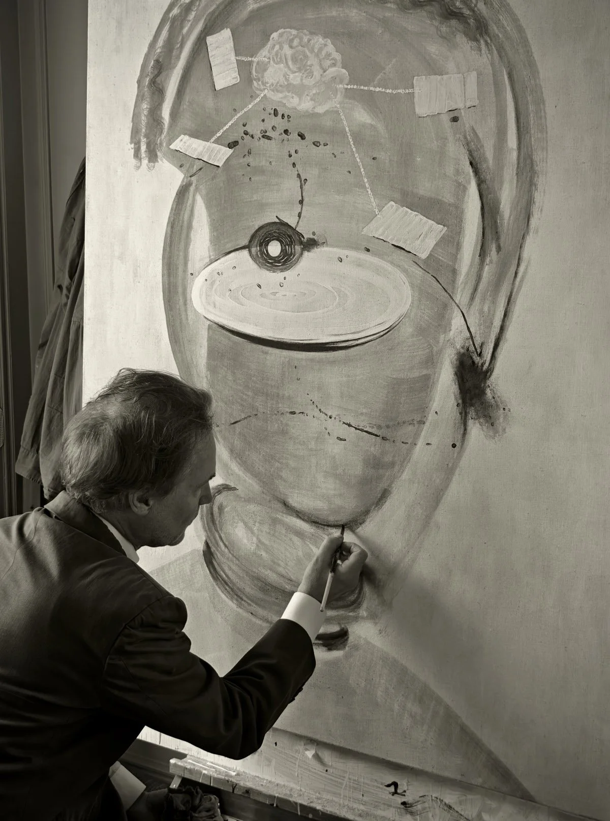 A man in a suit is painting a large abstract face on a wall, focusing on the eye area with a paintbrush.