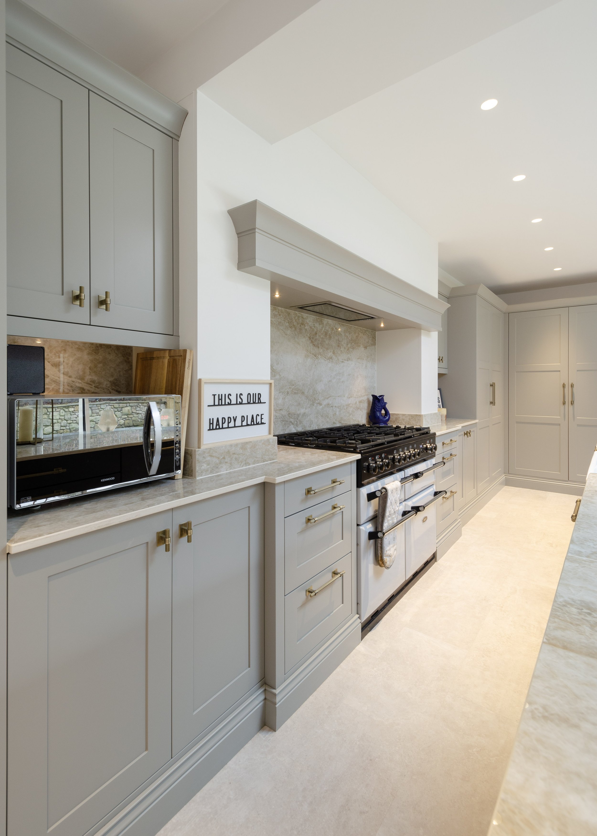 Bright kitchen with beige cabinets, a black stove, marble countertops, and a sign that reads 'This is our happy place'.