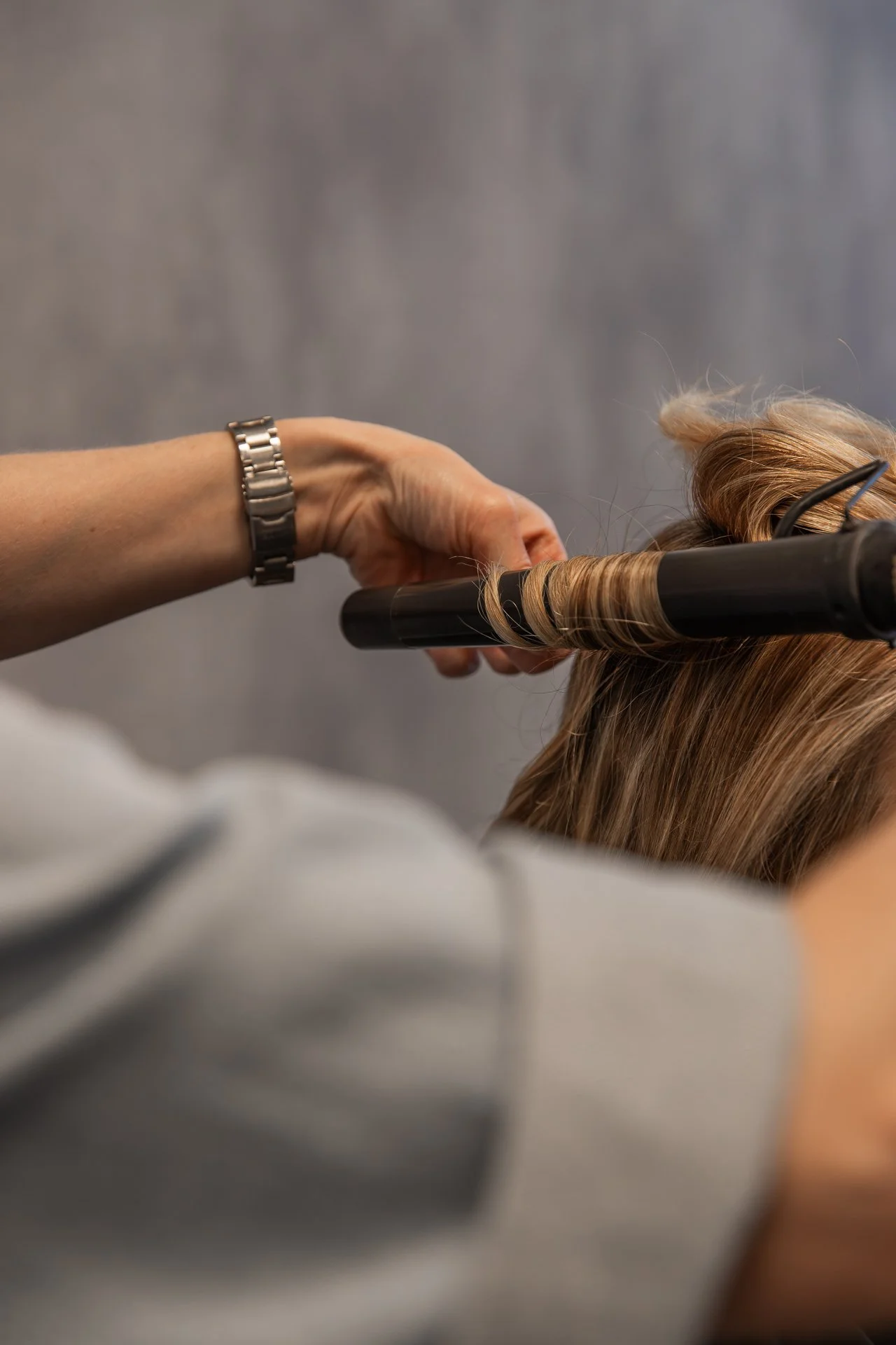 A person using a curling iron to curl blonde hair.